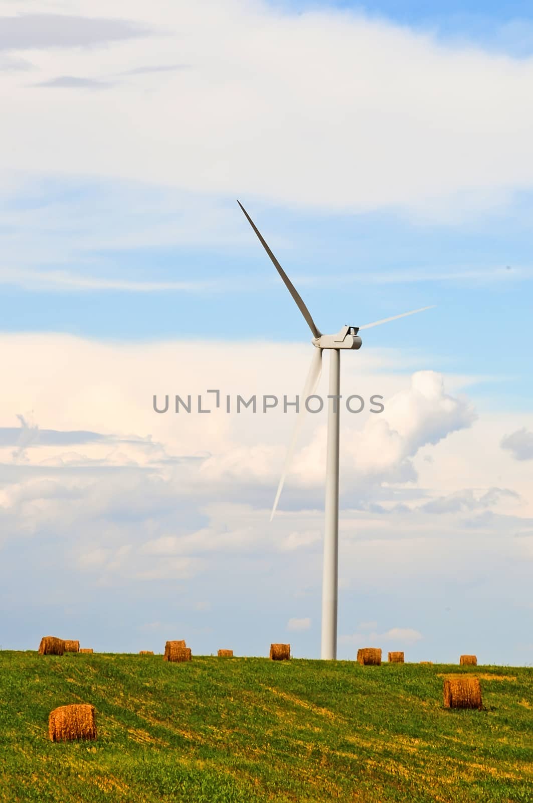 Wind turbines share a field with bales of straw as two renewable resources co-exist on the same land.