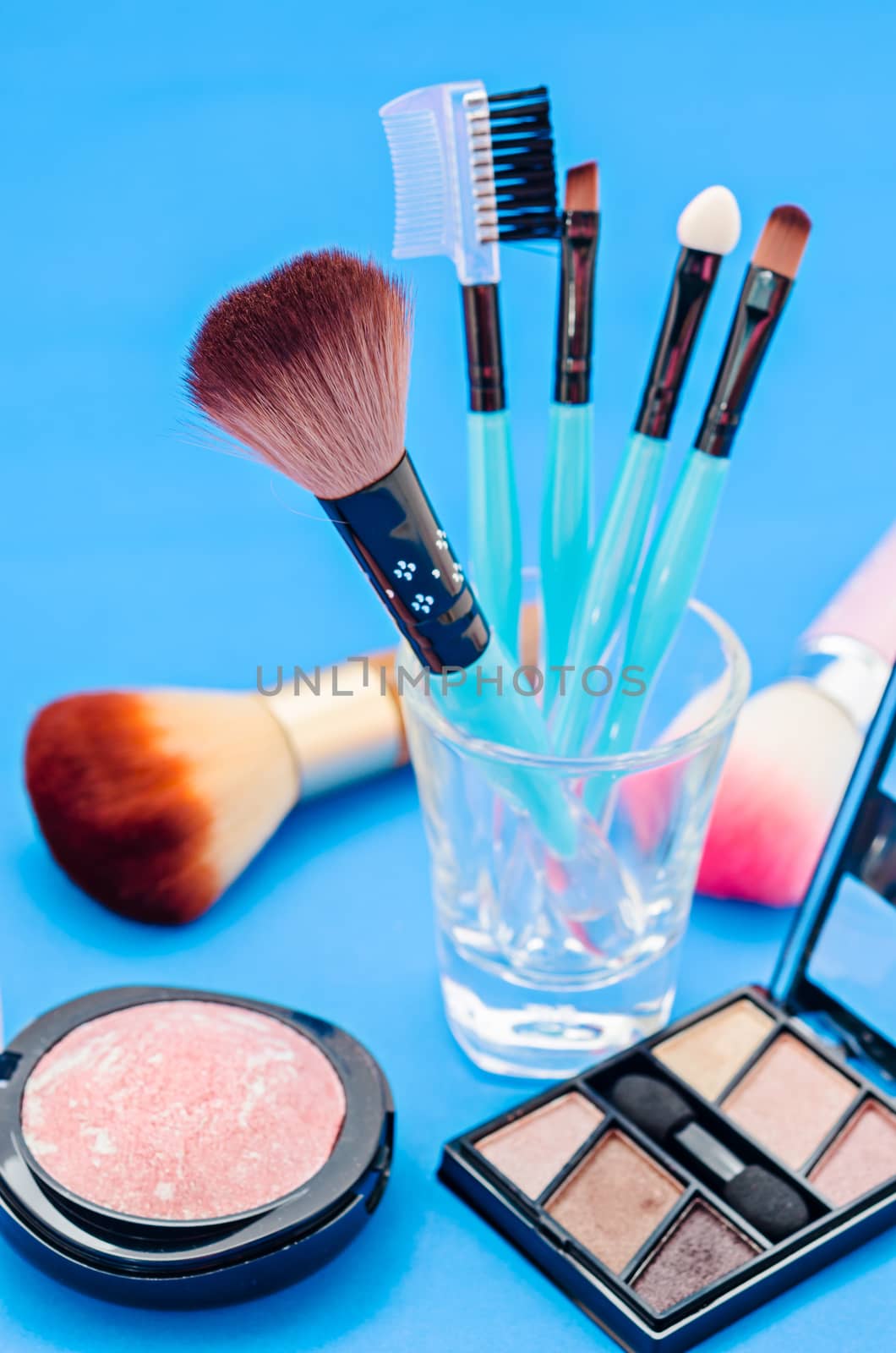 Makeup brush and cosmetics on blue background.