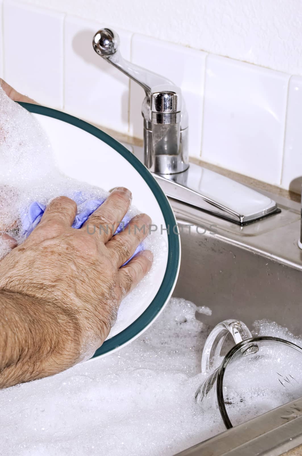 Hand washing a dinner plate in the kitchen sink.