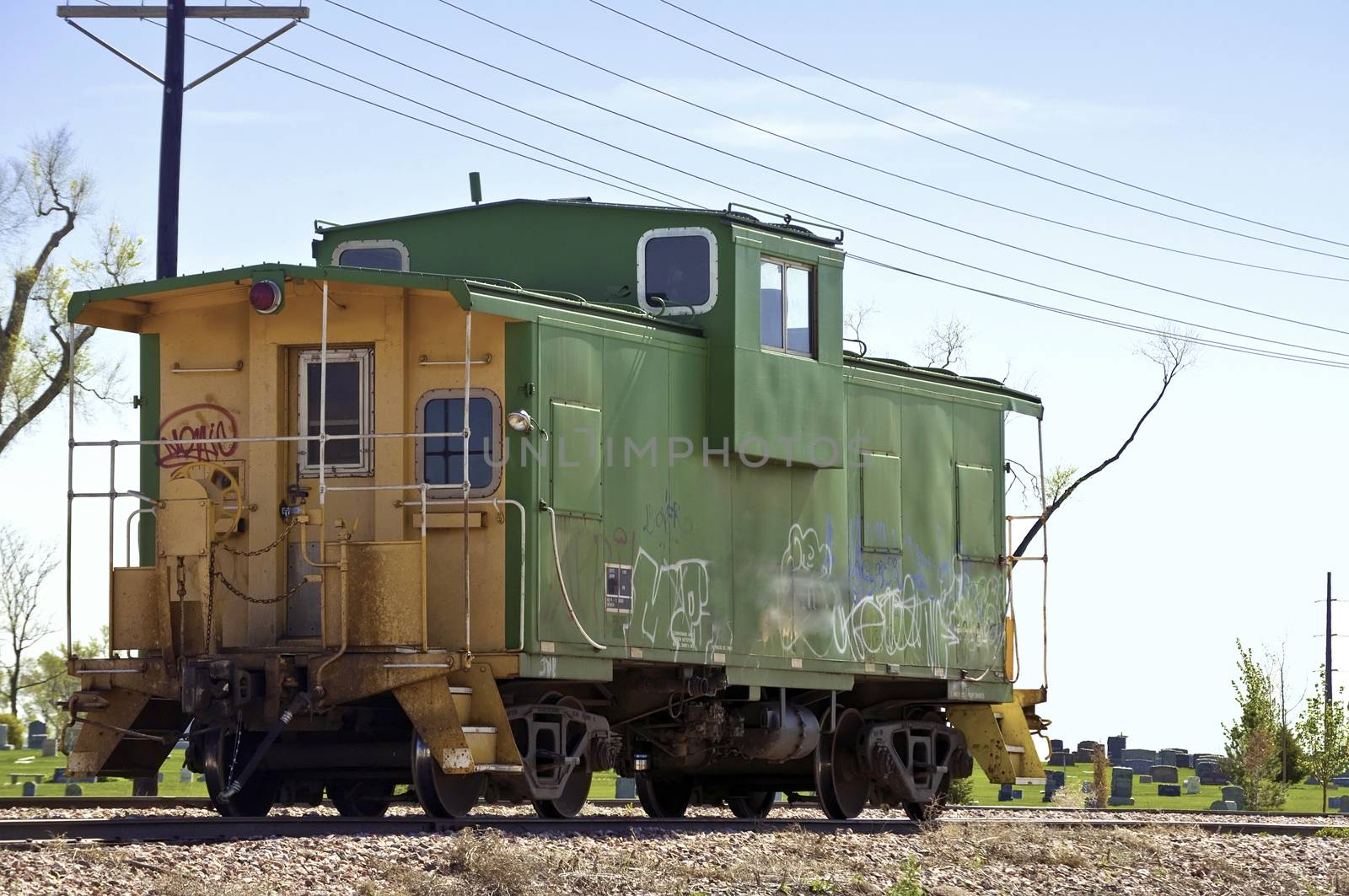 Railrolad caboose sits on a siding gathering grafitti near a cemetary.