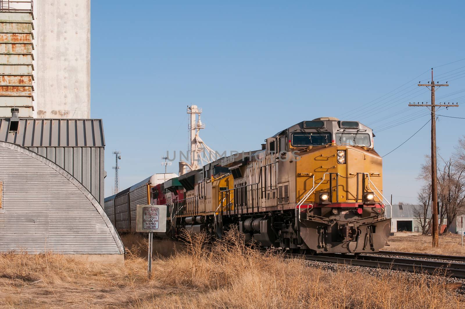 Freight train loaded with automobiles in covered transport cars traveling through a small rural Colorado town in the USA