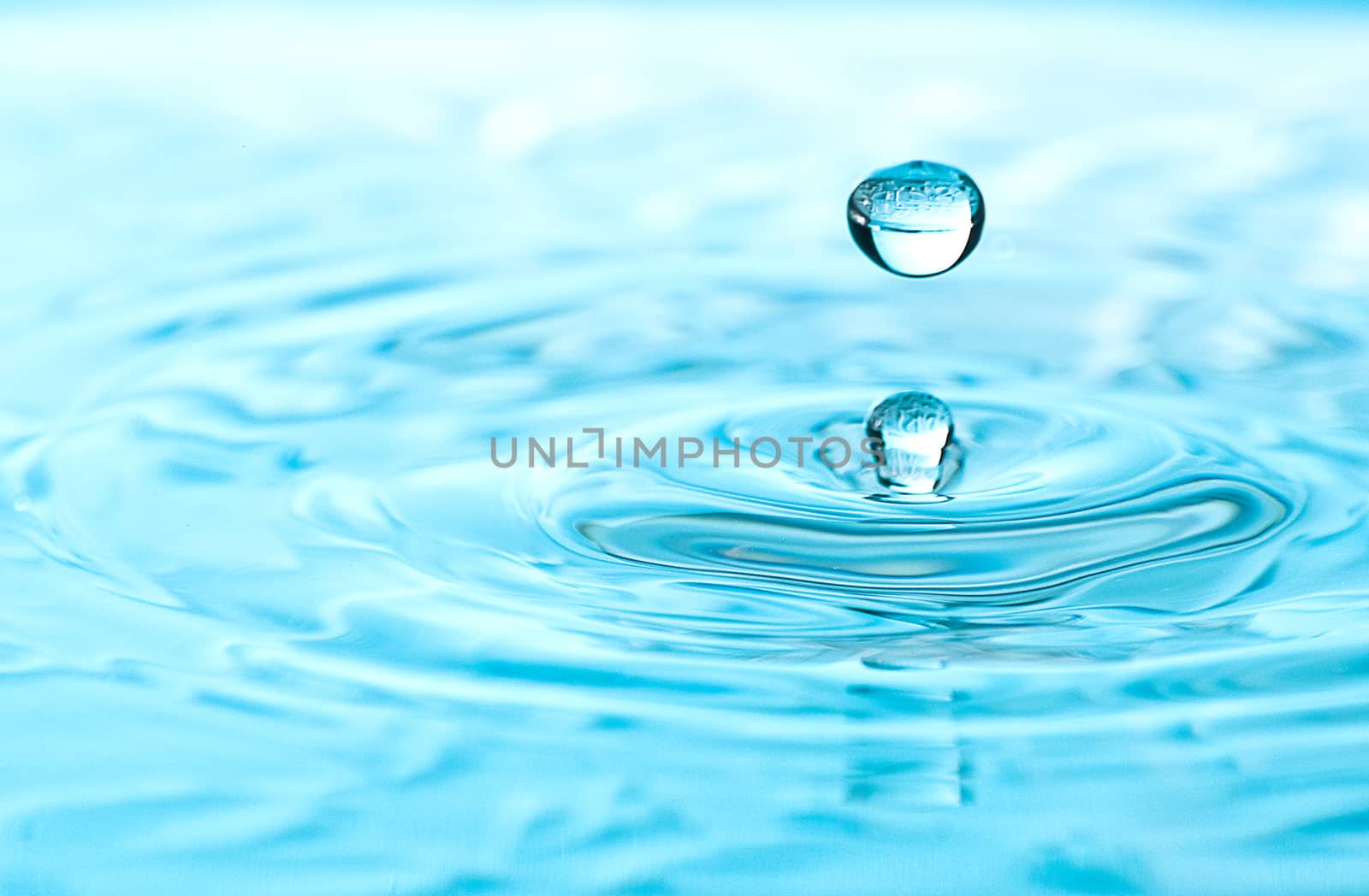 Water drop with clear reflection suspended above clear aqua colored pool