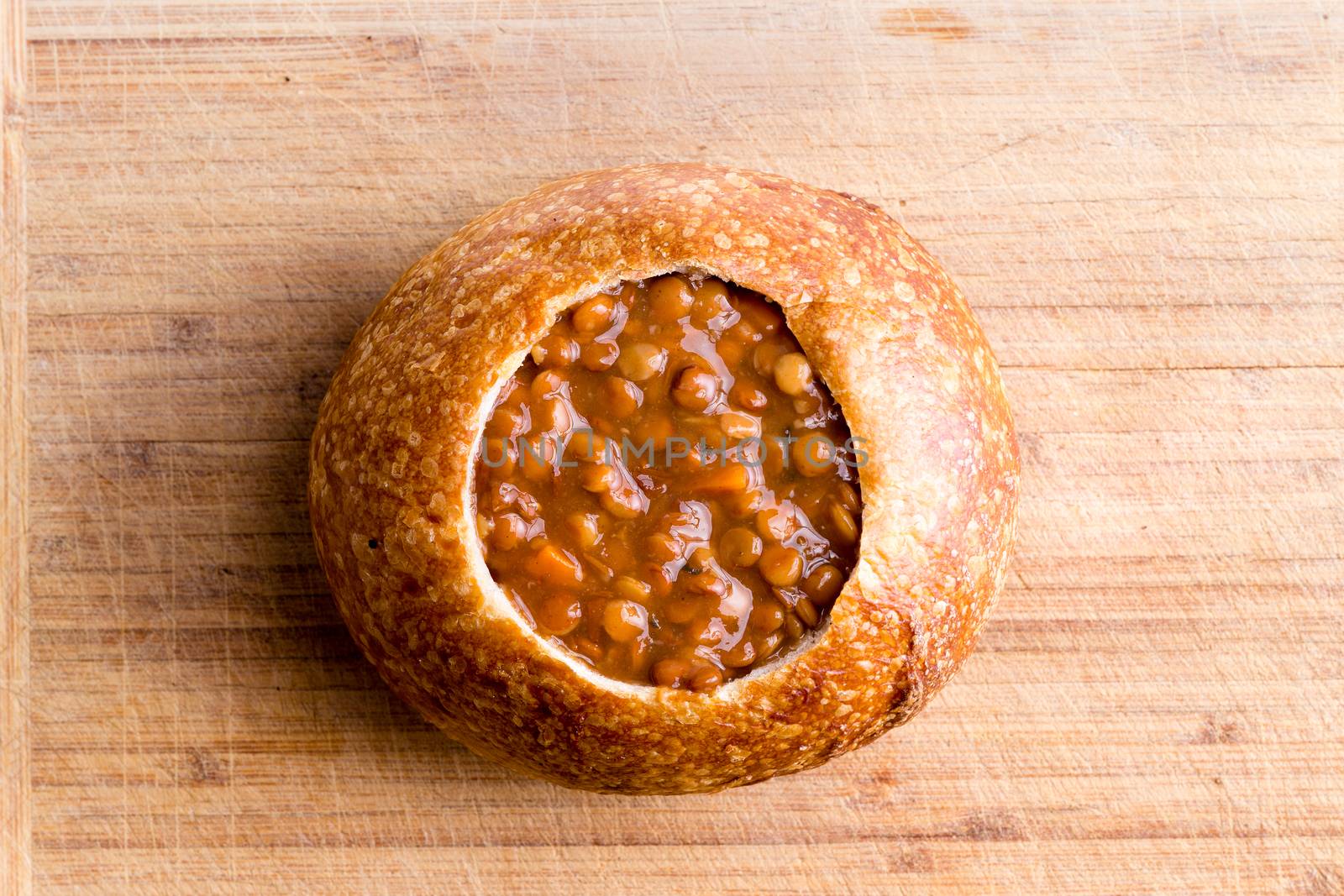 Lentil soup served in a sourdough bread bowl ready to be garnished in the kitchen, overhead view on a bamboo chopping board with copy space