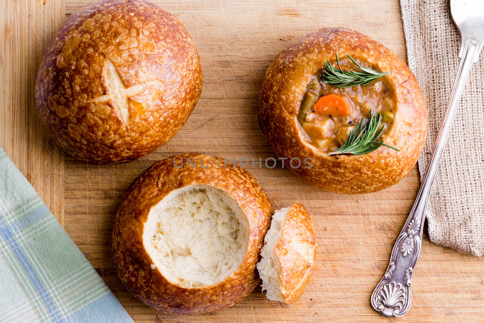 Stages in serving fresh vegetable soup in a sourdough bread bowl showing the whole bun, hollowed out and with the soup served in it, overhead view