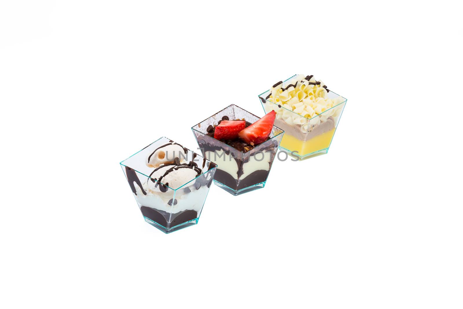 Arranged in a row diagonally,three cupcakes with choccolate,white choccolate, fruits,cream and custard in a plastic cup,isolated on white background.