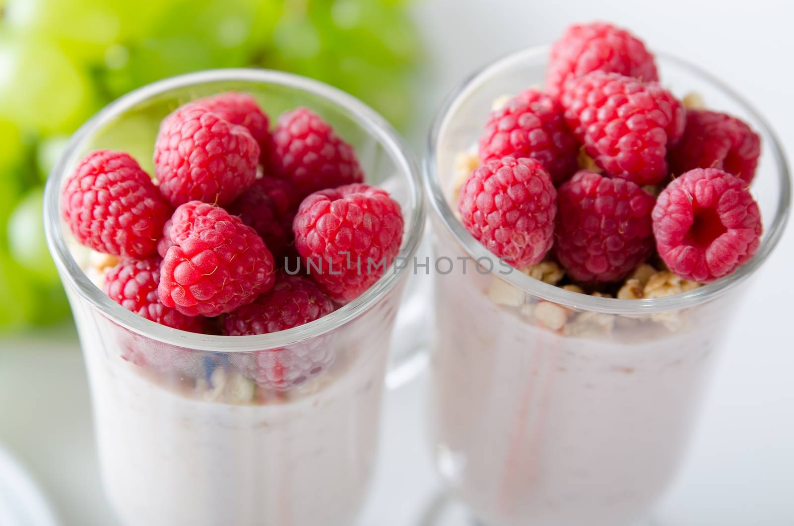 Glass of dessert with yoghurt, fresh berries and muesli. Grapes in background