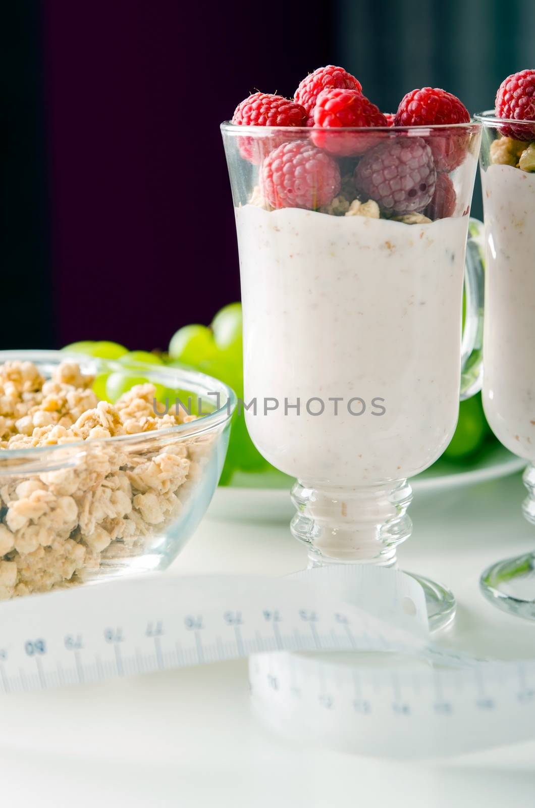 Glass of dessert with yoghurt, fresh berries and muesli. Grapes in background