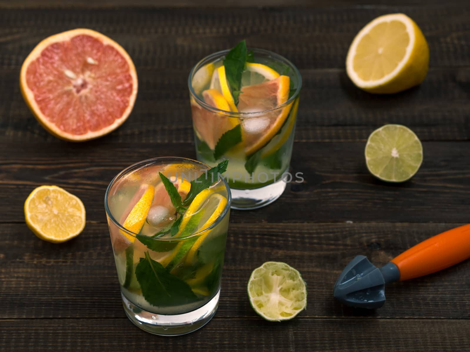 Cold homemade lemonade with fresh lemon, lime, grapefruit and mint by lemon reamer. Summer drink on dark wooden background