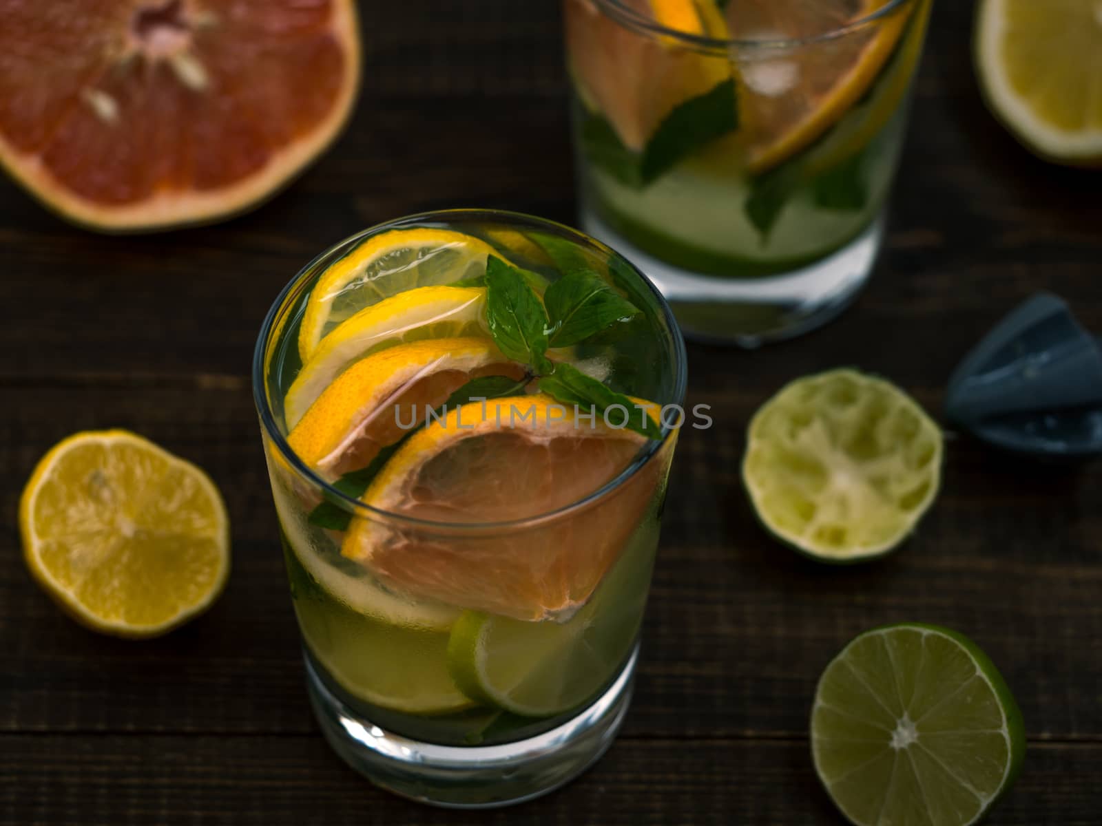 Cold homemade lemonade with fresh lemon, lime, grapefruit and mint by lemon reamer. Summer drink on dark wooden background