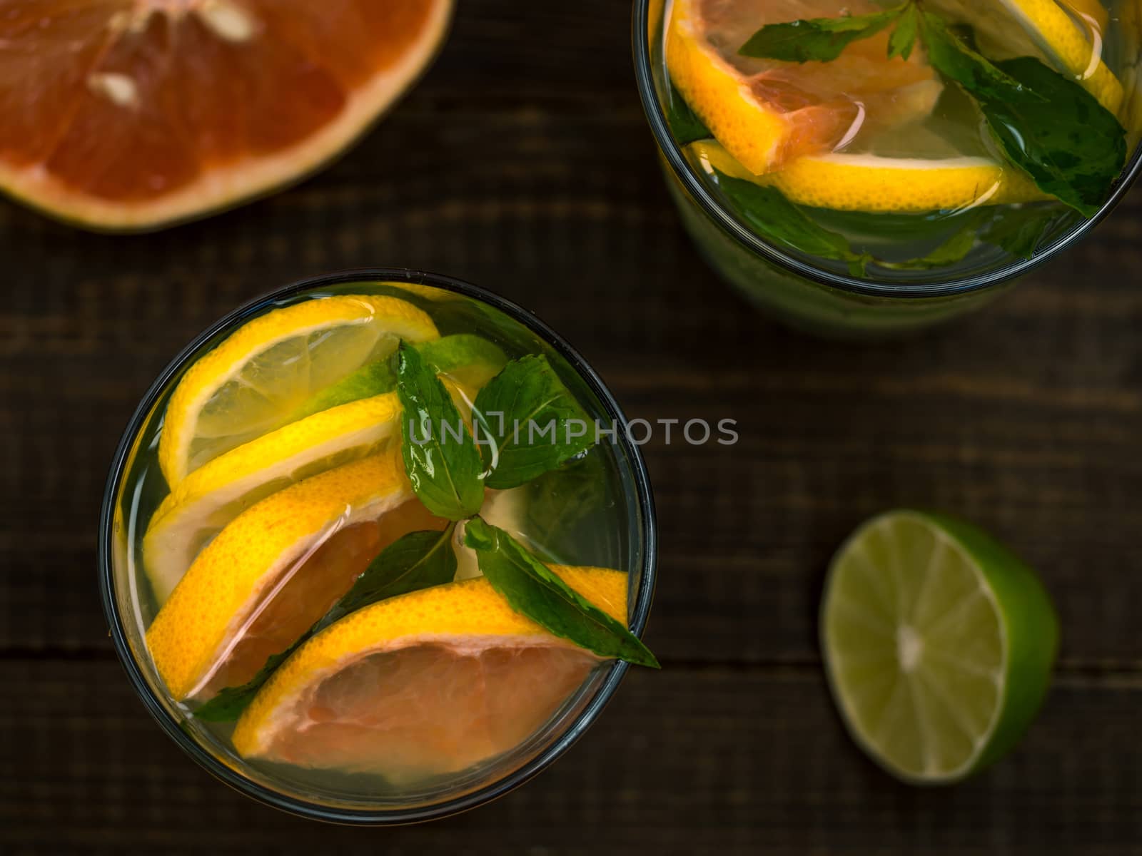 Closeup cold homemade lemonade with fresh lemon, lime, grapefruit and mint. Summer drink on dark wooden background. Flat lay or top view