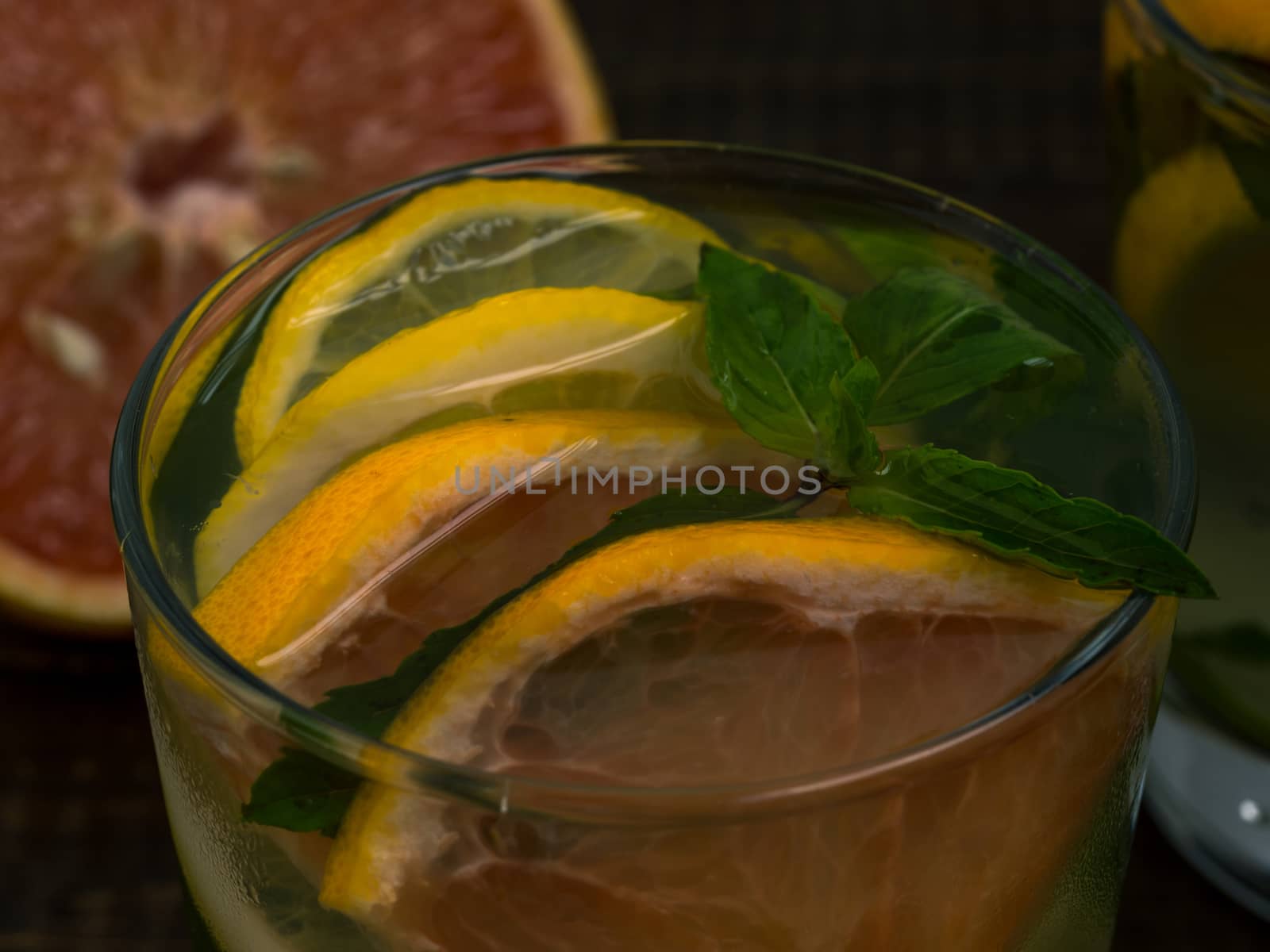 Close up cold homemade lemonade with fresh lemon, lime, grapefruit and mint. Summer drink on dark wooden background