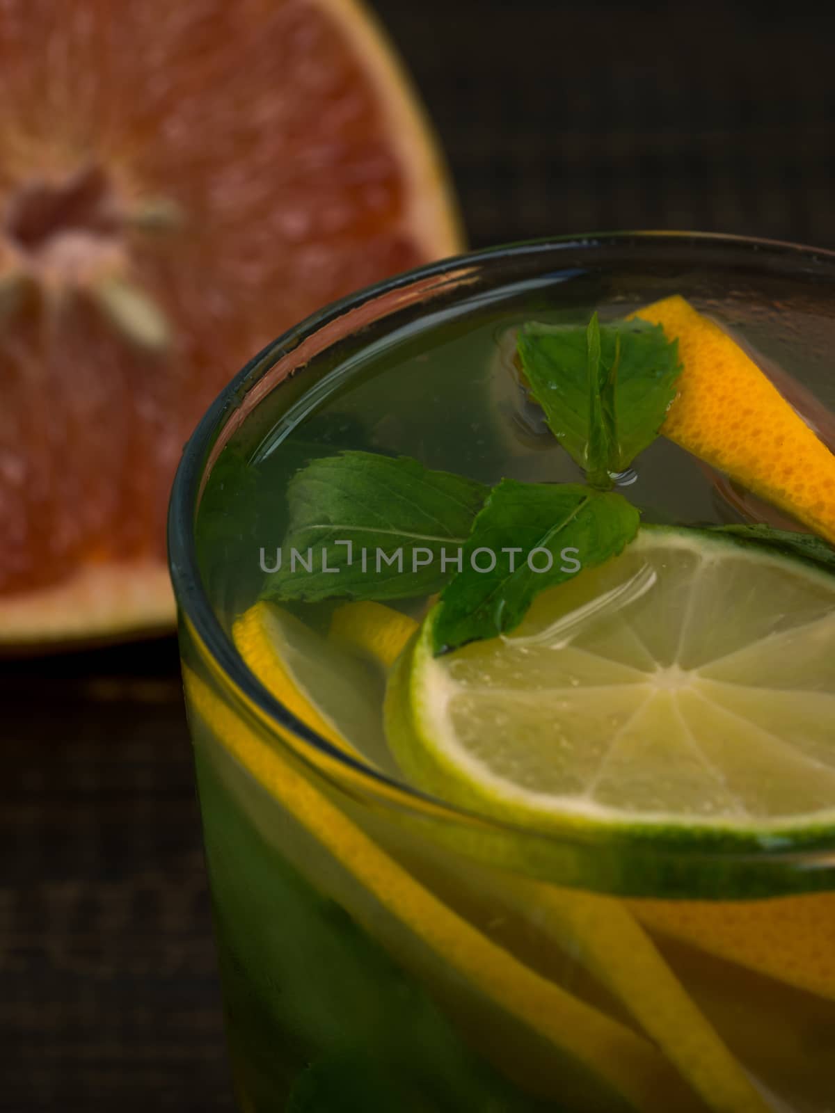 Close up cold homemade lemonade with fresh lemon, lime, grapefruit and mint. Summer drink on dark wooden background. Vertical