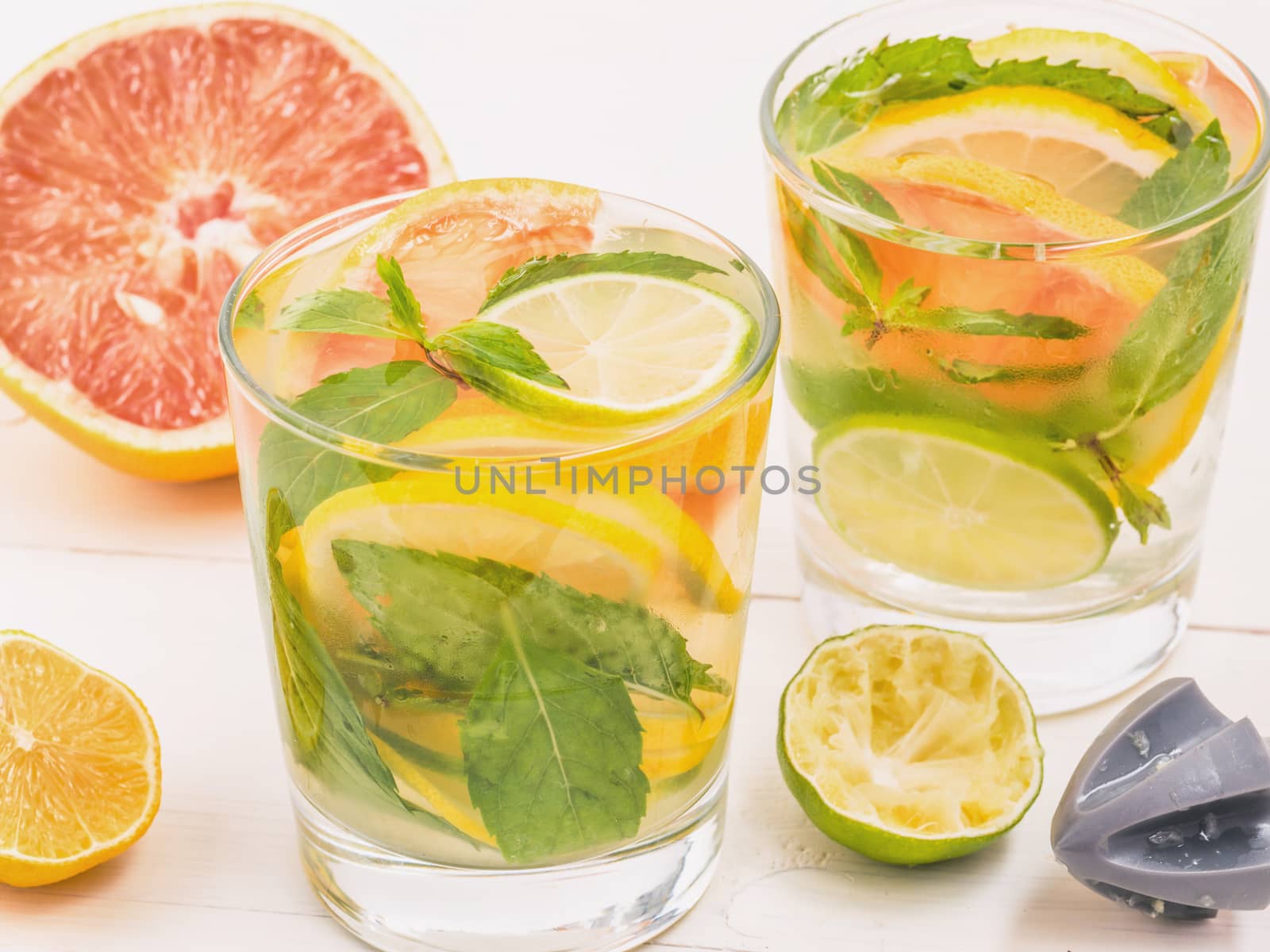 Cold homemade lemonade with fresh lemon, lime, grapefruit and mint by lemon reamer. Summer drink on white wooden background