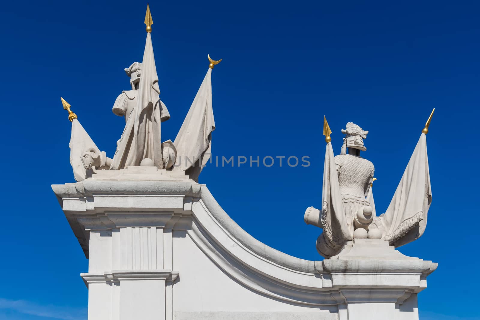 Detail of a gate at the castle in Bratislava, Slovakia, which is part of UNESCO World Heritage site. Statues with flags. Bright blue summer sky.