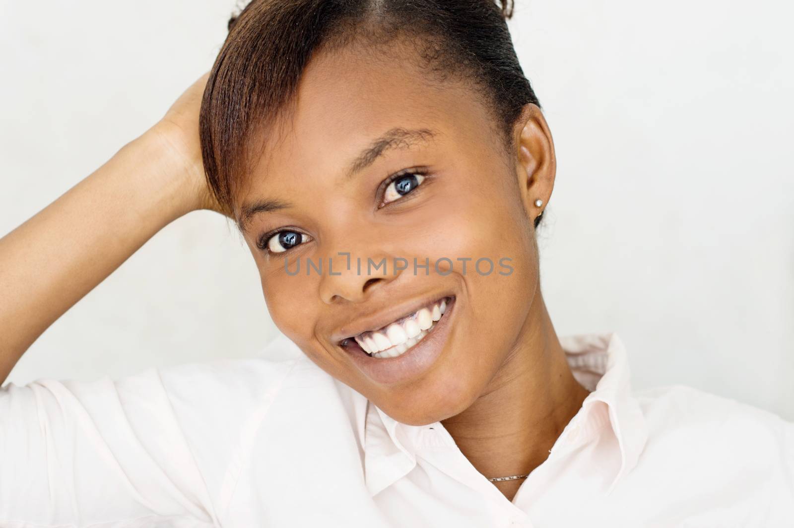 young woman sitting and holding her head with her right hand, looks at the camera with a beautiful smile