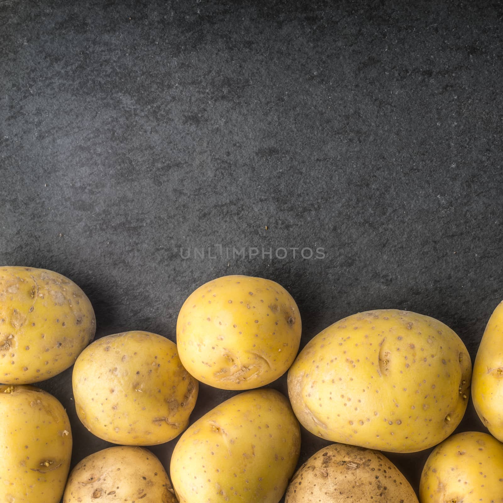 Raw potatoes on the black stone table square