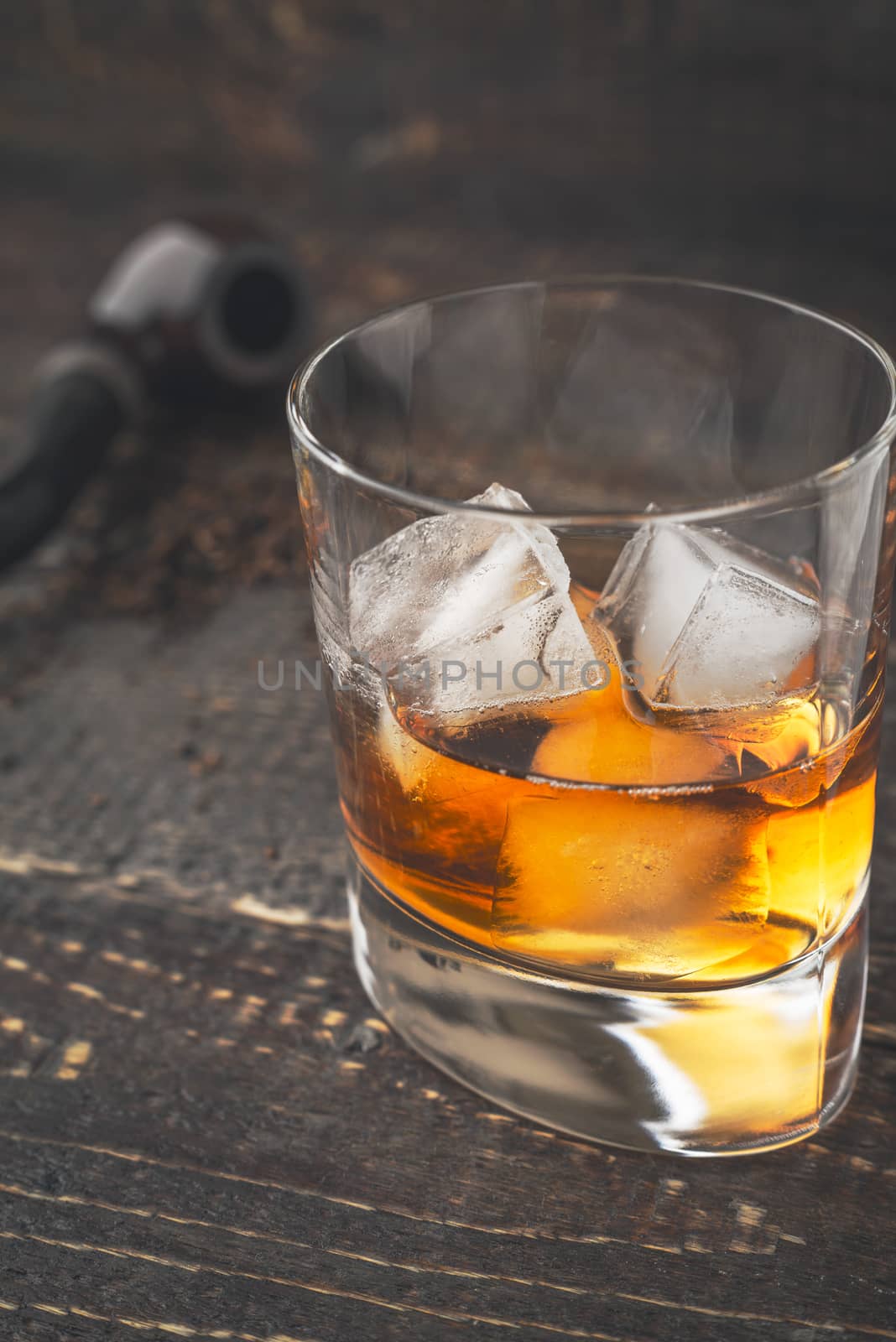 Whiskey with ice  and blurred pipe vertical