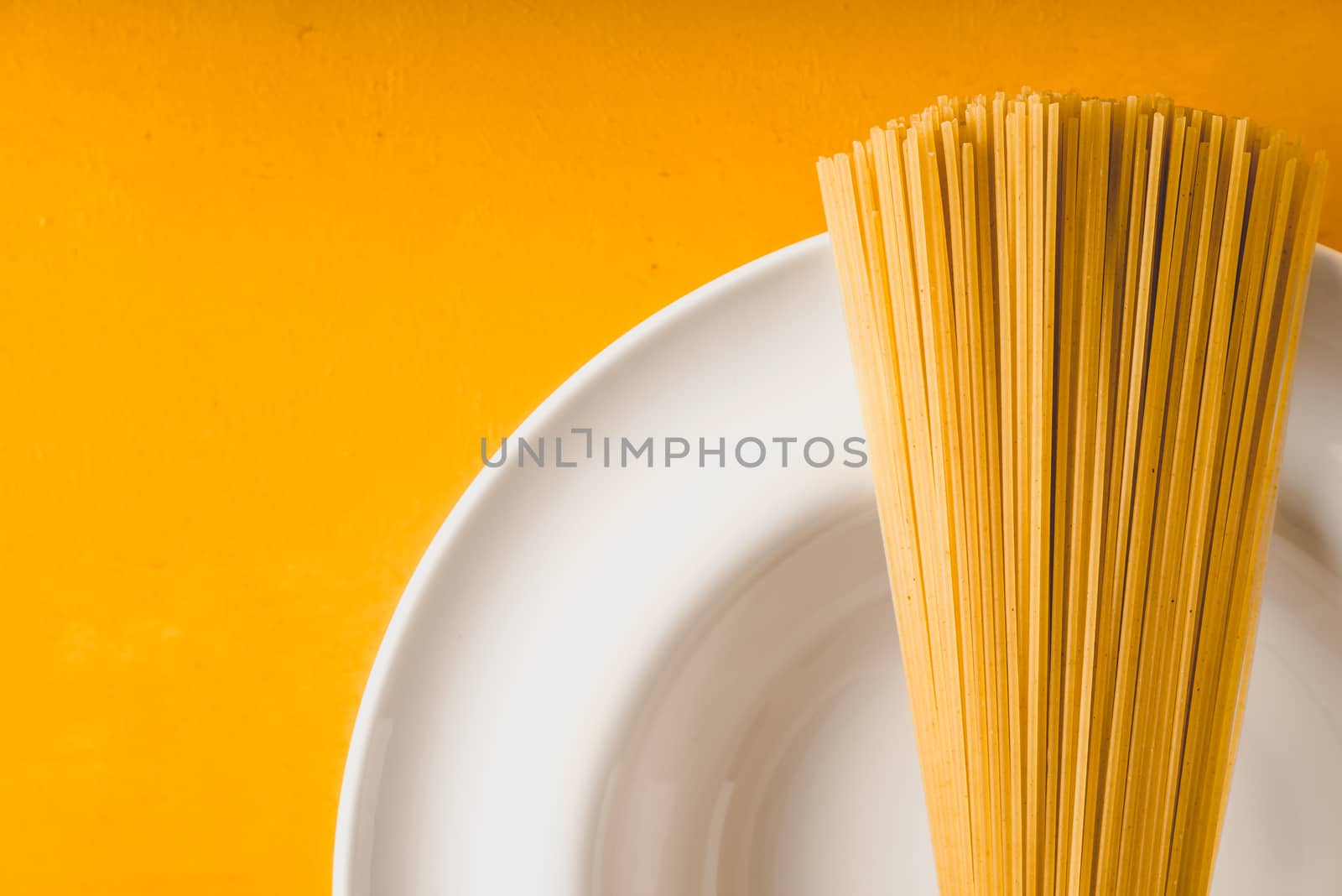 Raw spaghetti  on the white plate on the yellow background