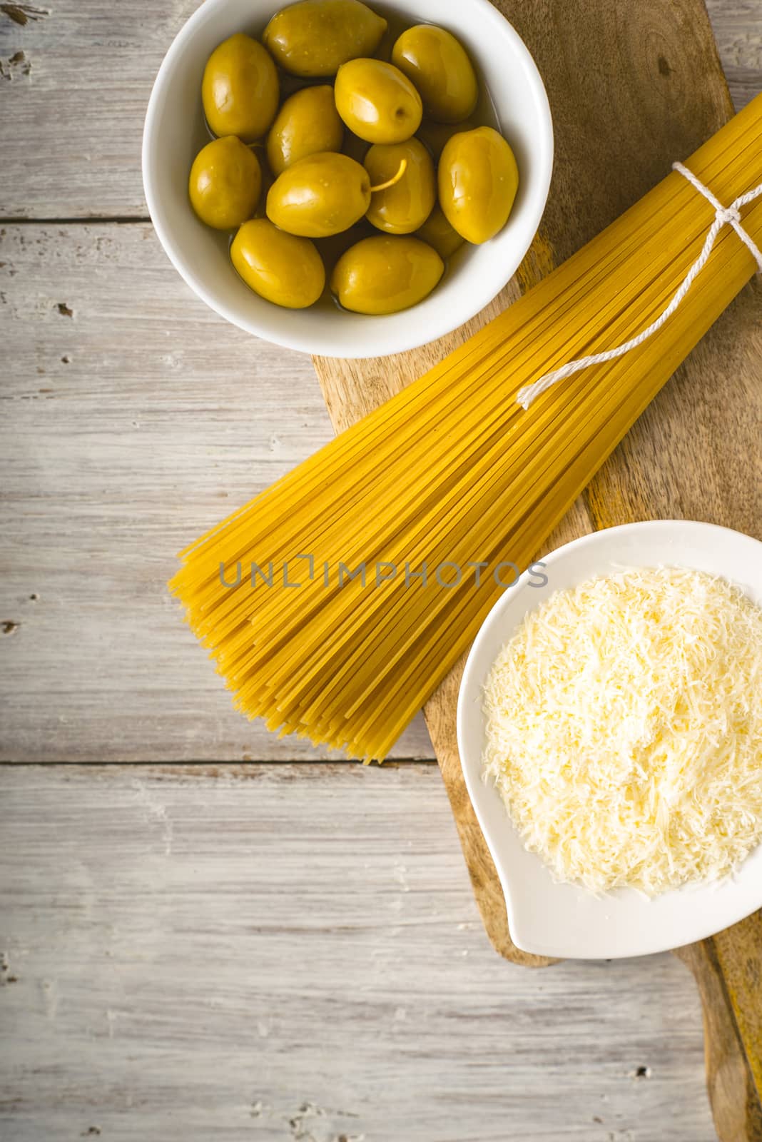 Raw spaghetti with olives and cheese on the white wooden table vertical by Deniskarpenkov