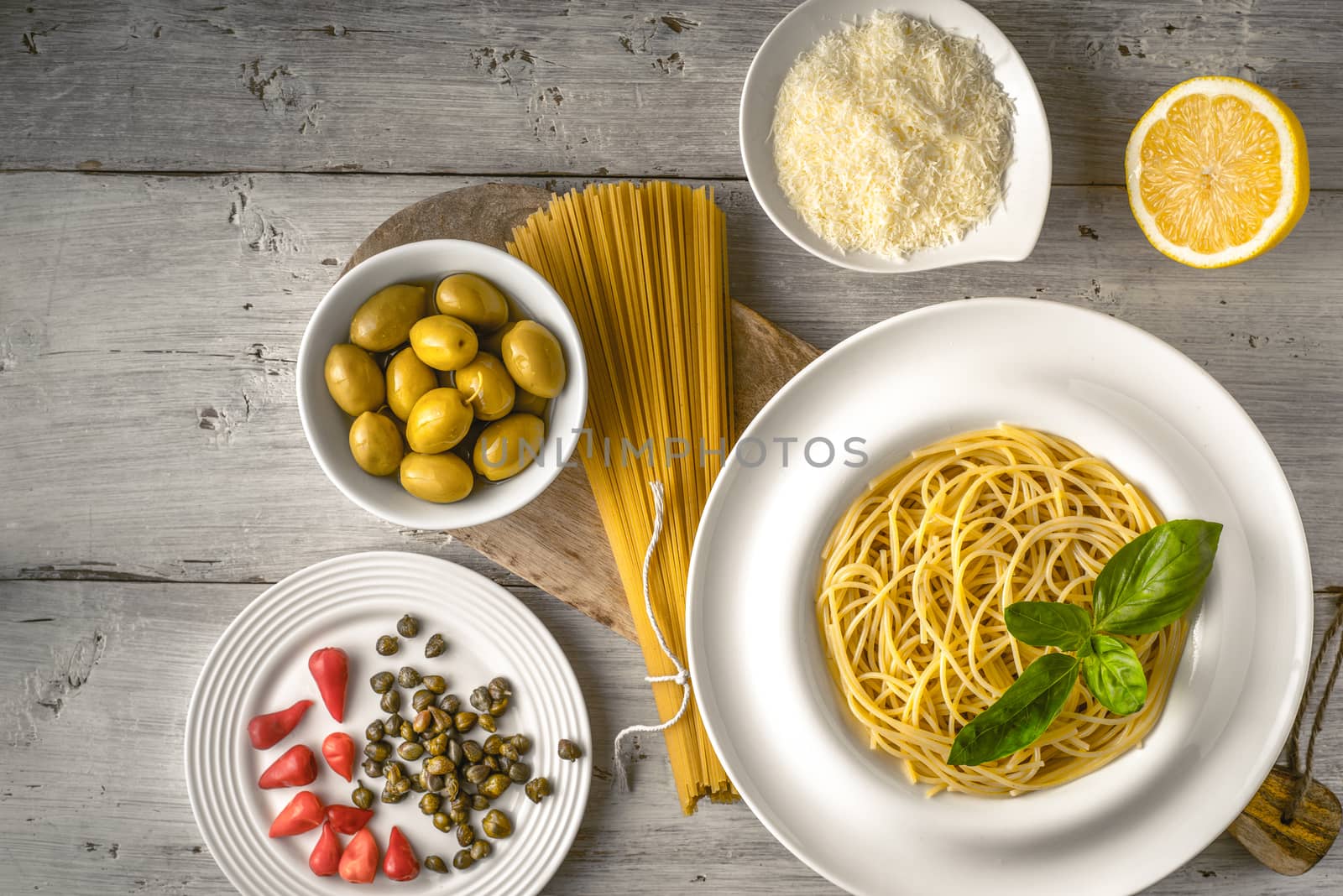 Raw and cooked spaghetti with different appetizer on the white wooden table top view. Concept of Italian cuisine