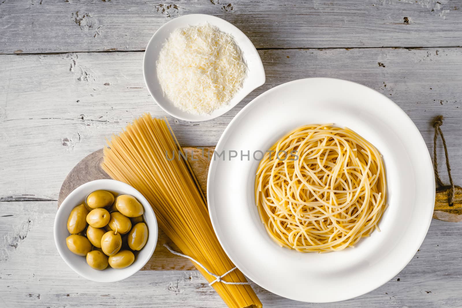 Raw and cooked spaghetti with olives and cheese on the white wooden table top view. Concept of Italian cuisine