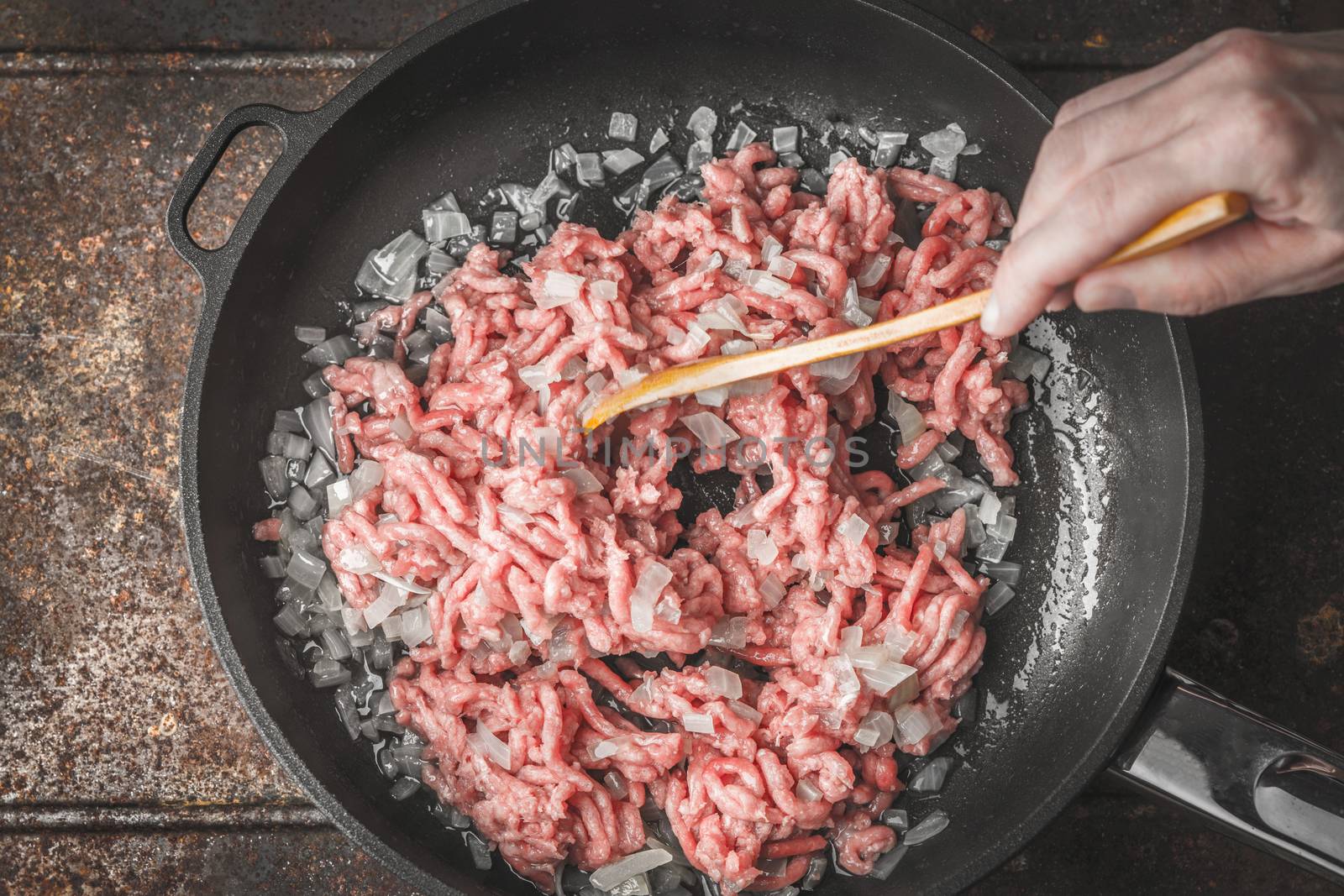 Raw minced meat with sliced onion in the pan with wooden spoon in the hand