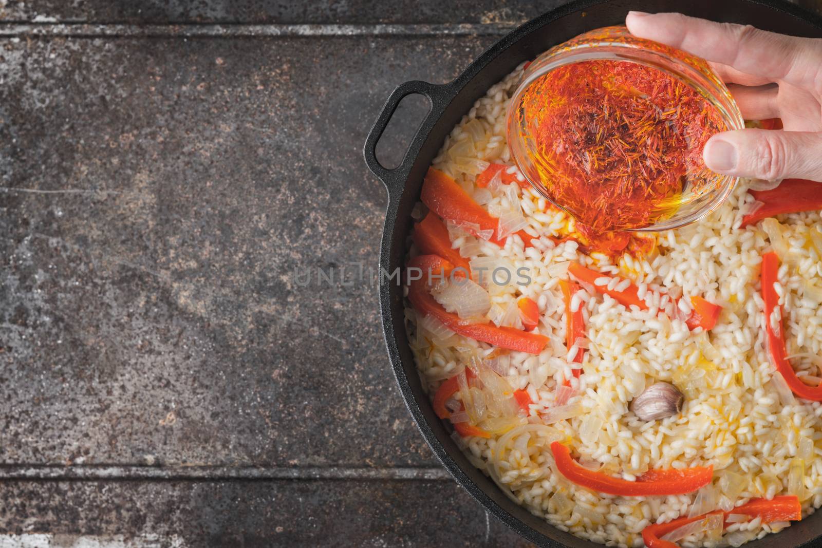 Adding saffron in the pan with rice and bell pepper top view by Deniskarpenkov