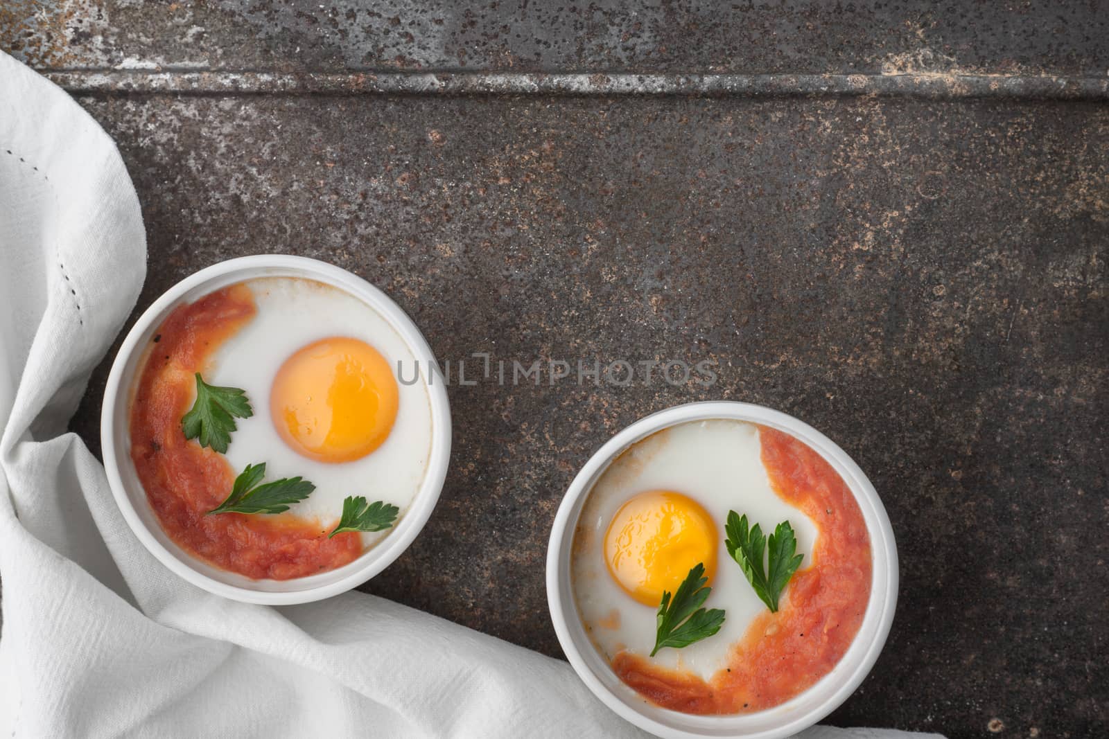 Eggs baked with tomatoes and parsley in the ramekins on the metal background top view