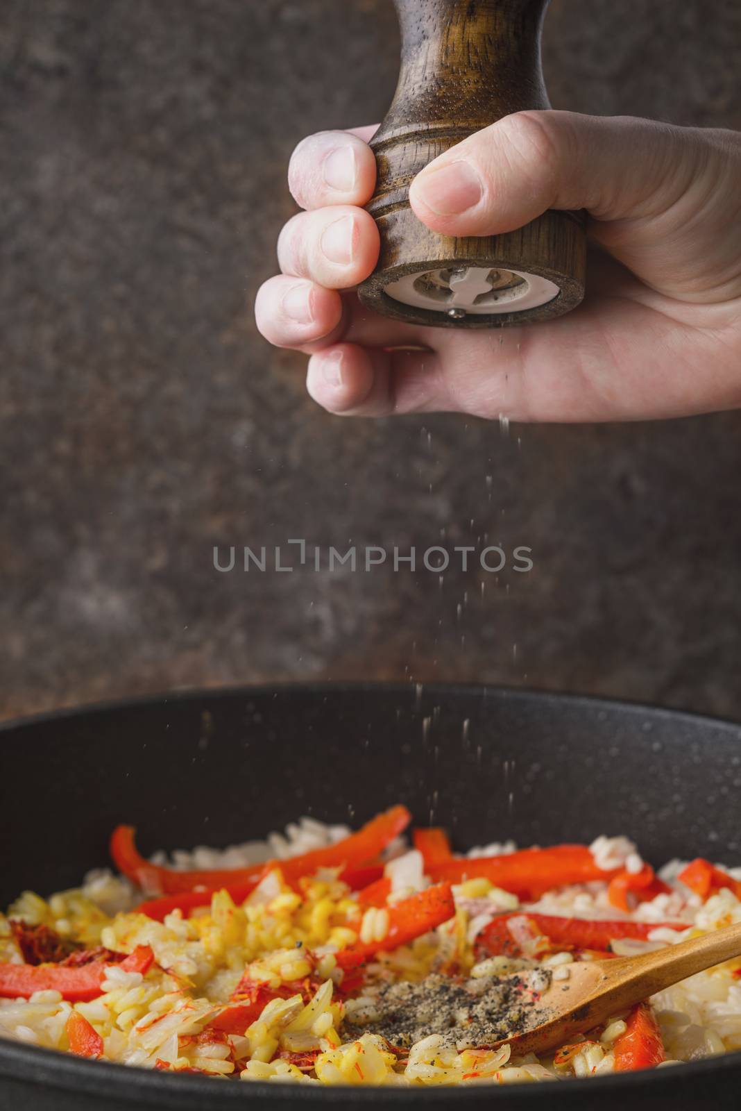 Adding black pepper in the pan with rice and bell pepper vertical by Deniskarpenkov