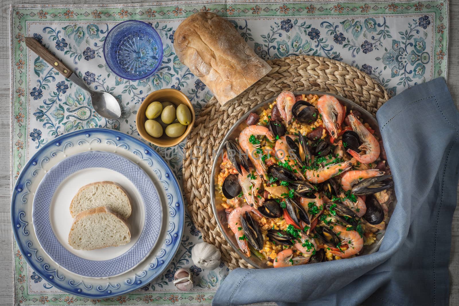 Paella on the metal plate on the beautiful napkin with tableware and bread top viewAC