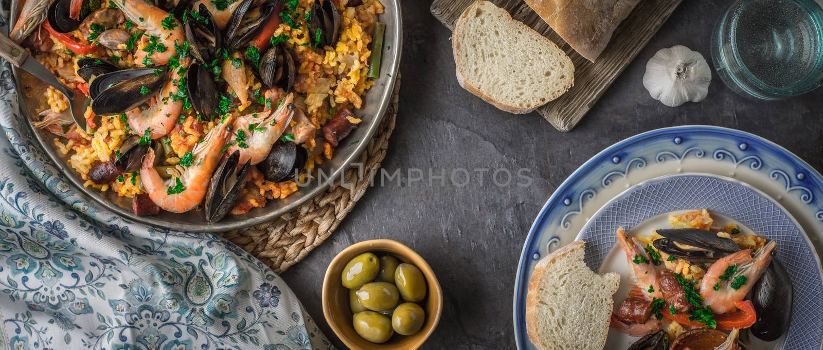 Plates with paella on the dark stone table with different accessories wide screen by Deniskarpenkov