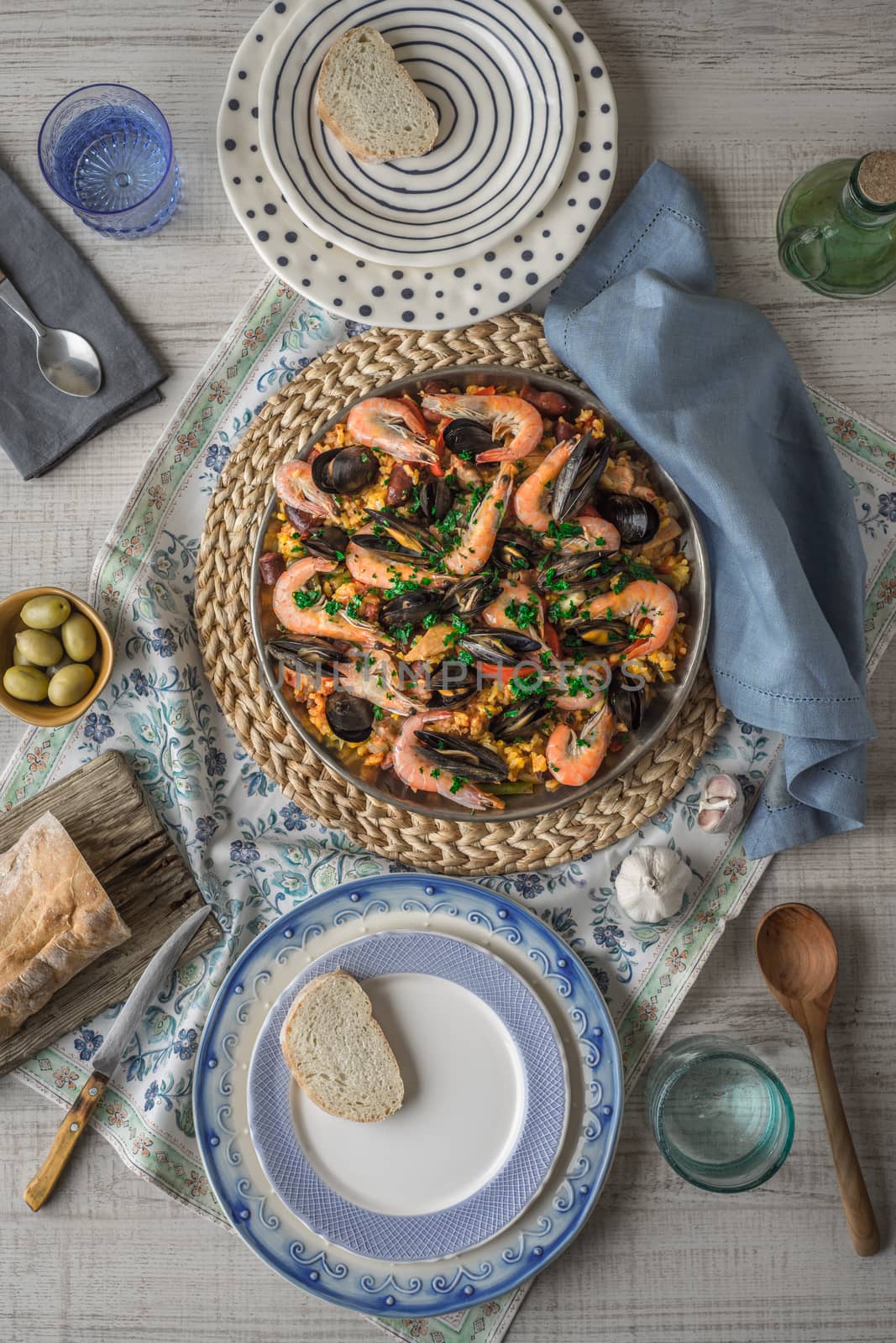Paella on the metal plate on the beautiful napkin with tableware and bread vertical by Deniskarpenkov