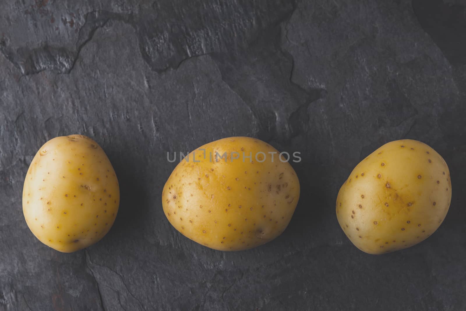 Potatoes on the dark stone table top view by Deniskarpenkov