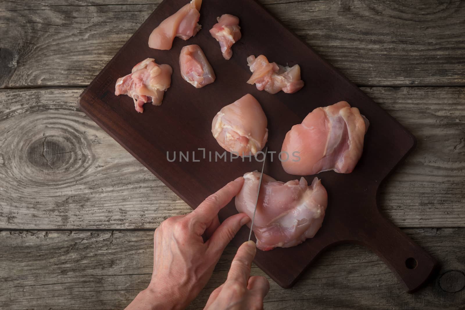 Cutting raw chicken fillet on the wooden board top view