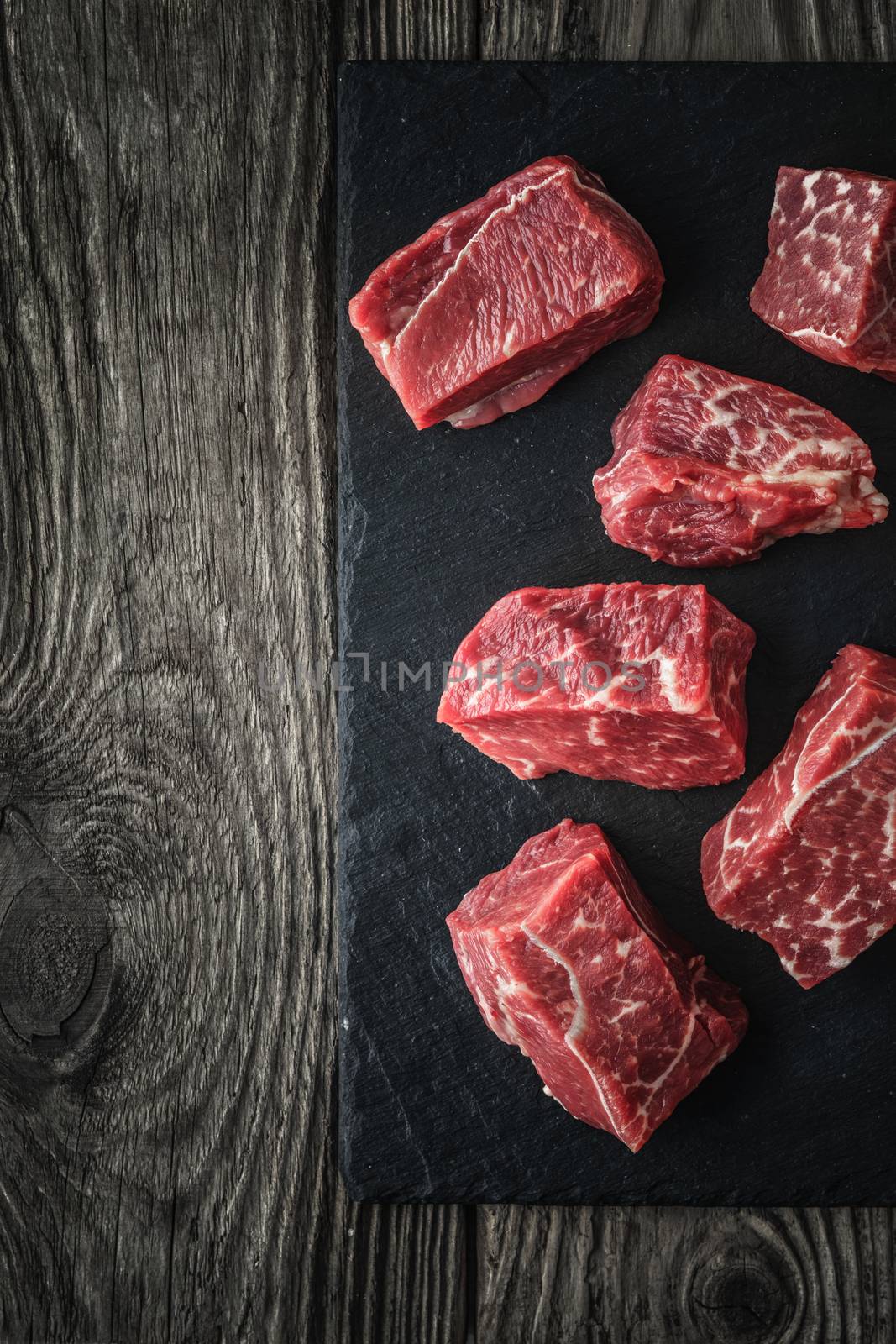 Raw angus beef slices on the black stone  on the wooden table vertical by Deniskarpenkov