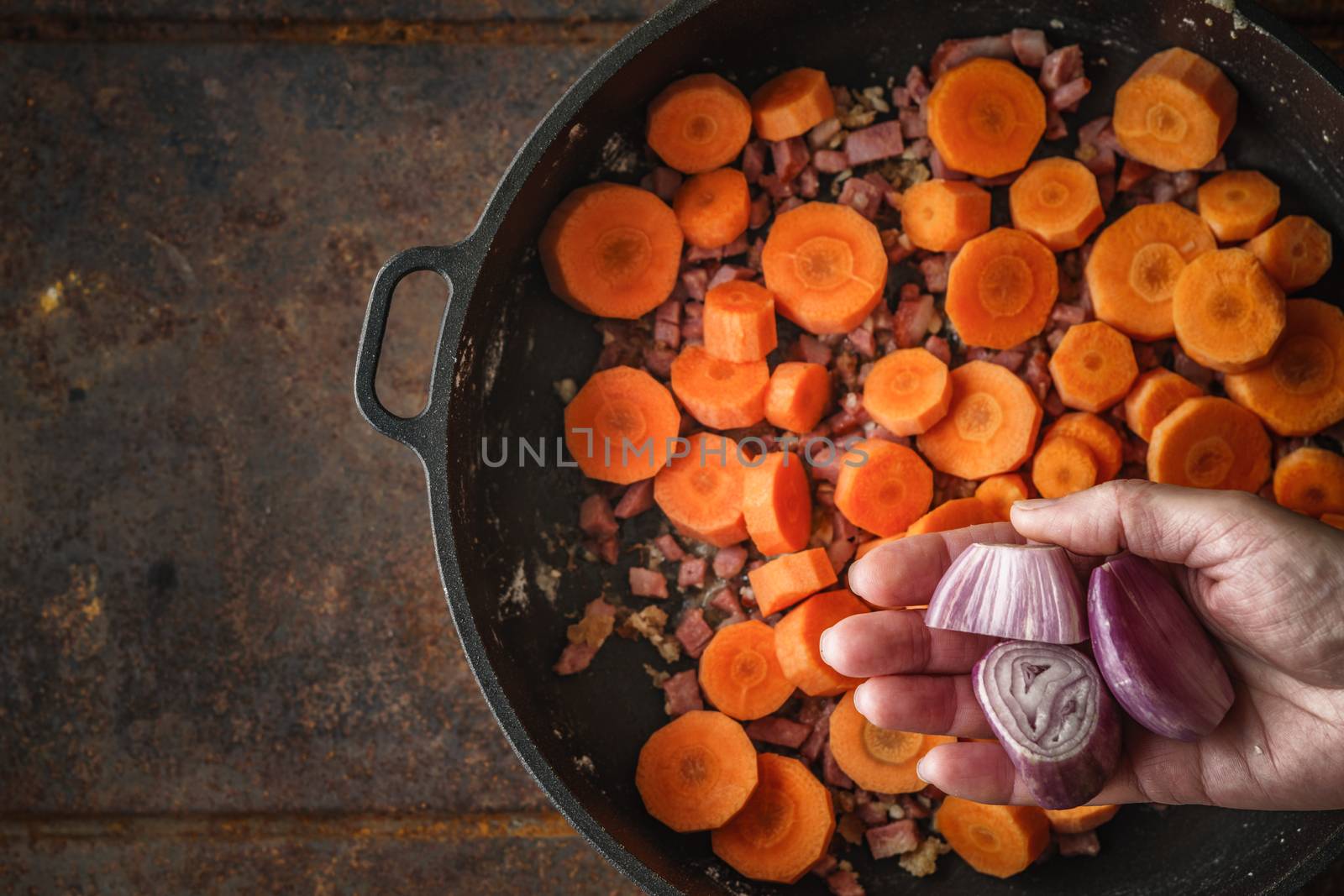 Adding shallot in the pan with bacon and carrots top view by Deniskarpenkov