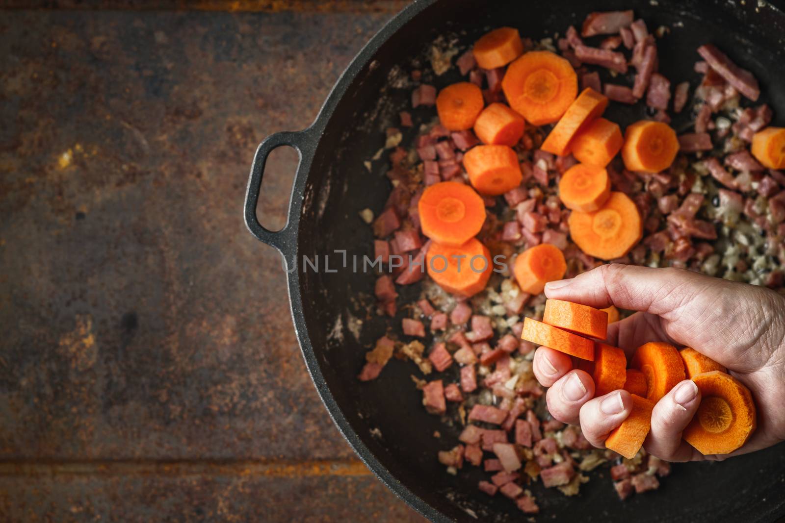 Adding carrots in the pan with bacon top view by Deniskarpenkov