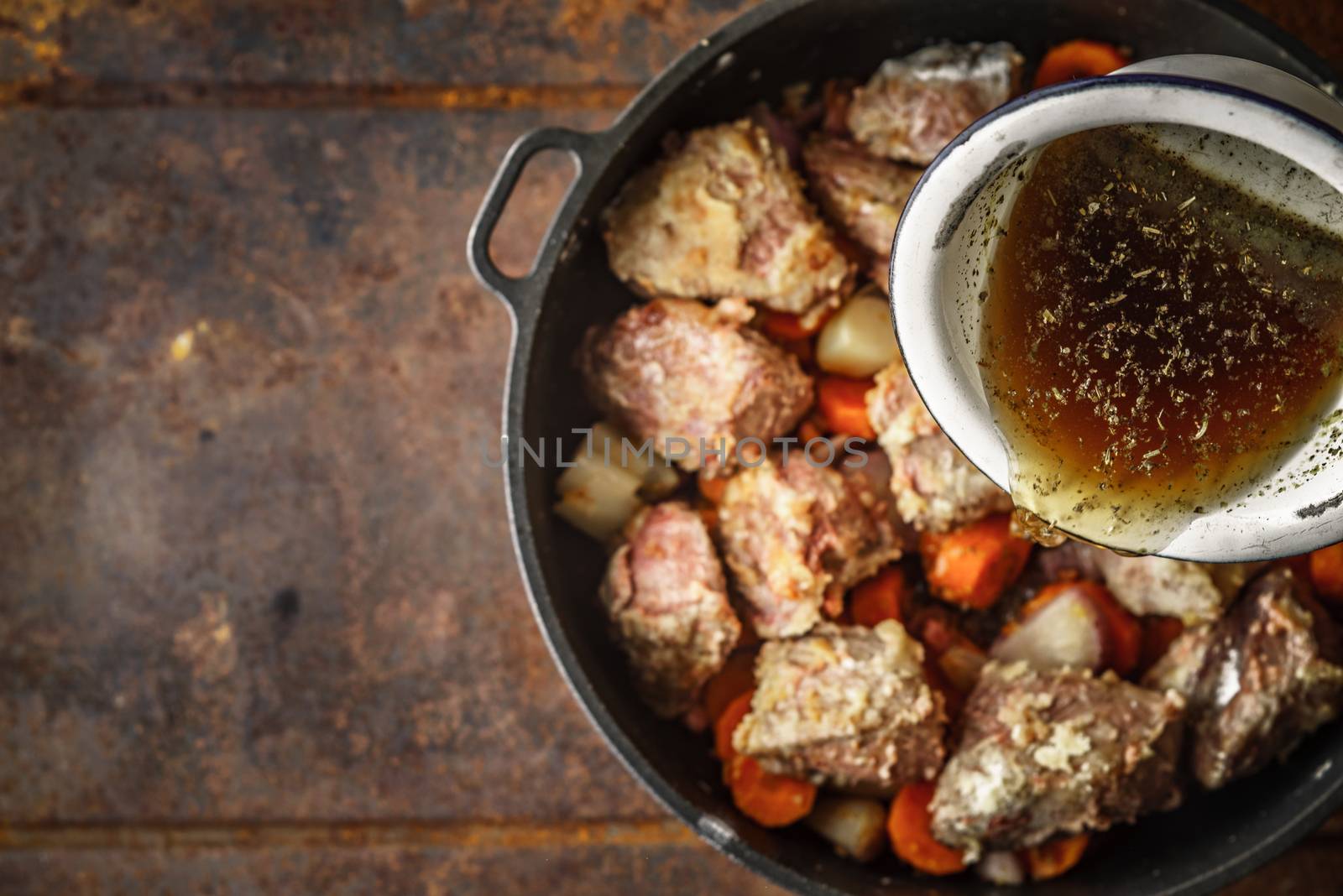 Adding broth in the pan with meat and vegetable top view by Deniskarpenkov