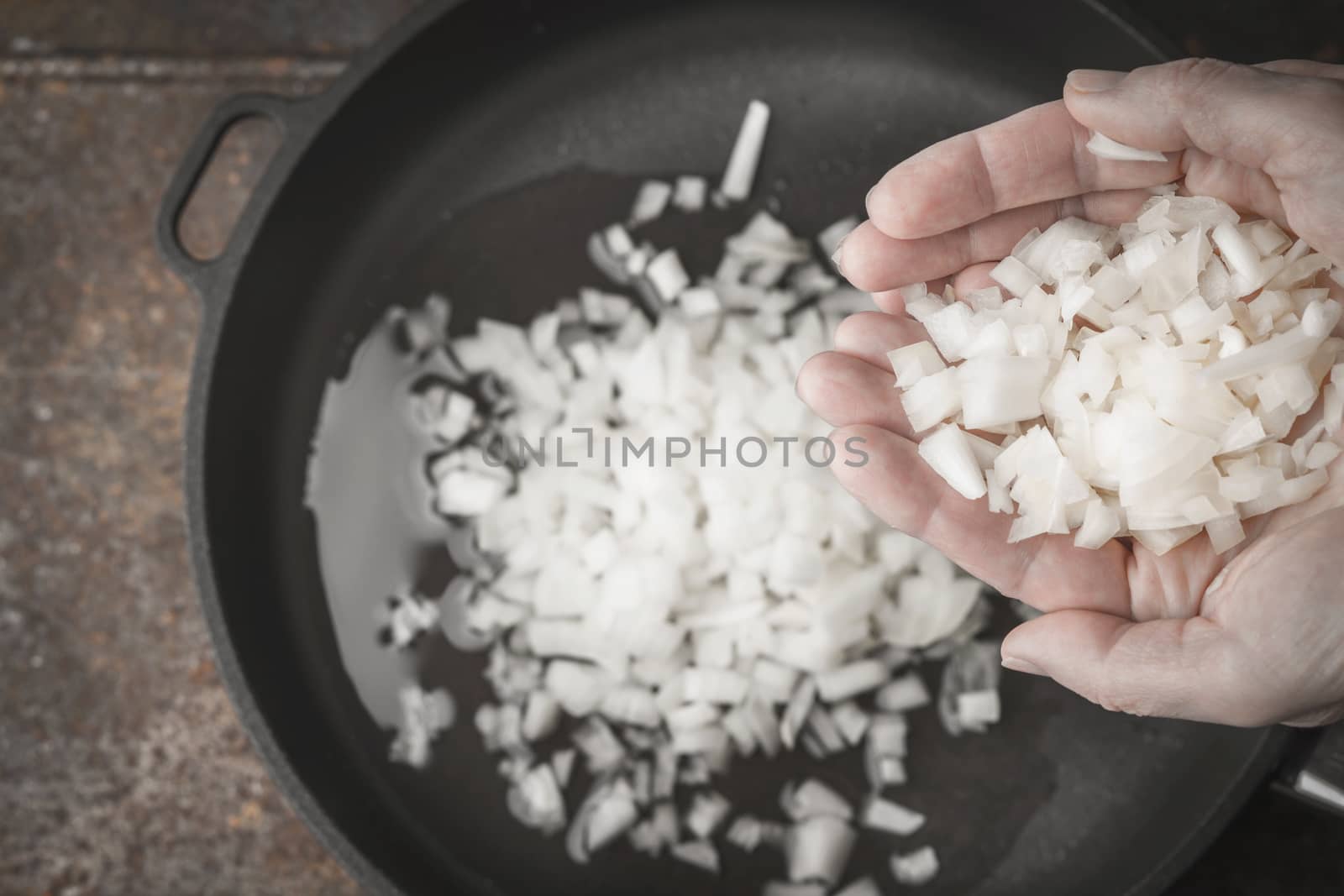 Sliced onion in the hand with blurred pan top view by Deniskarpenkov