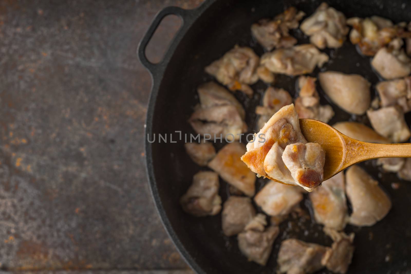 Fried chicken in the wooden spoon with blurred pan by Deniskarpenkov