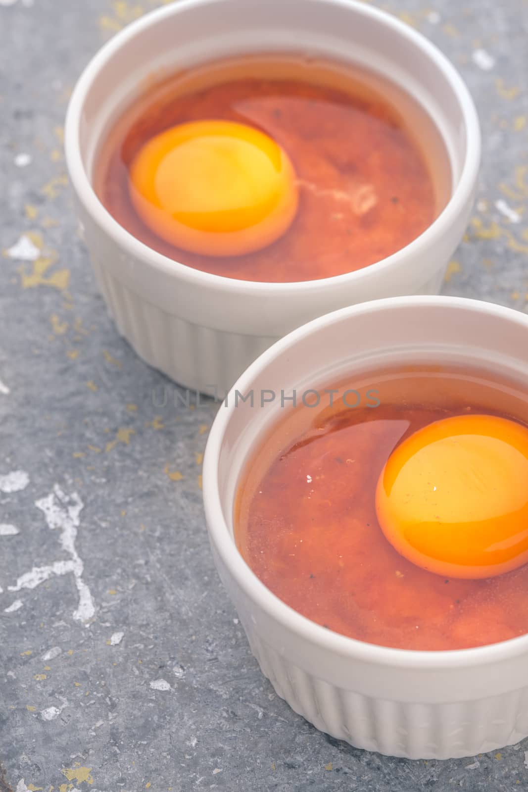Raw eggs with tomatoes in the ramekins on the stone table vertical