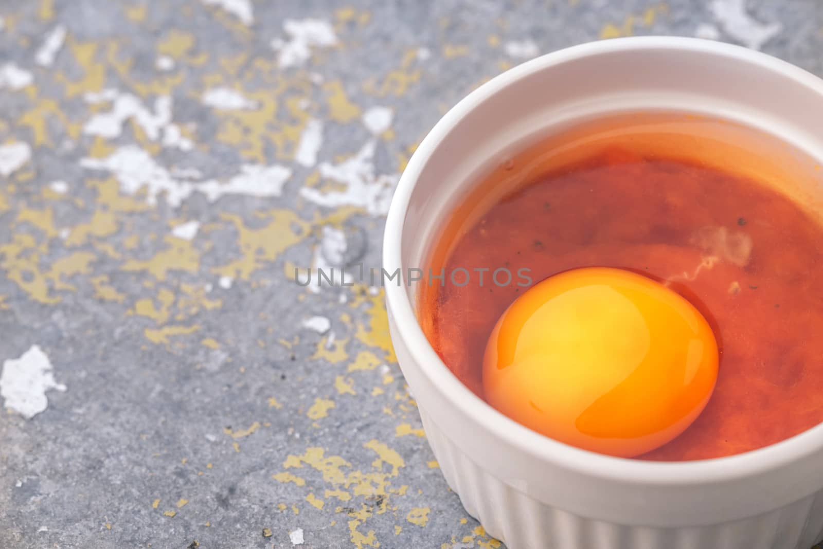 Raw eggs with tomatoes in the ramekins on the stone table