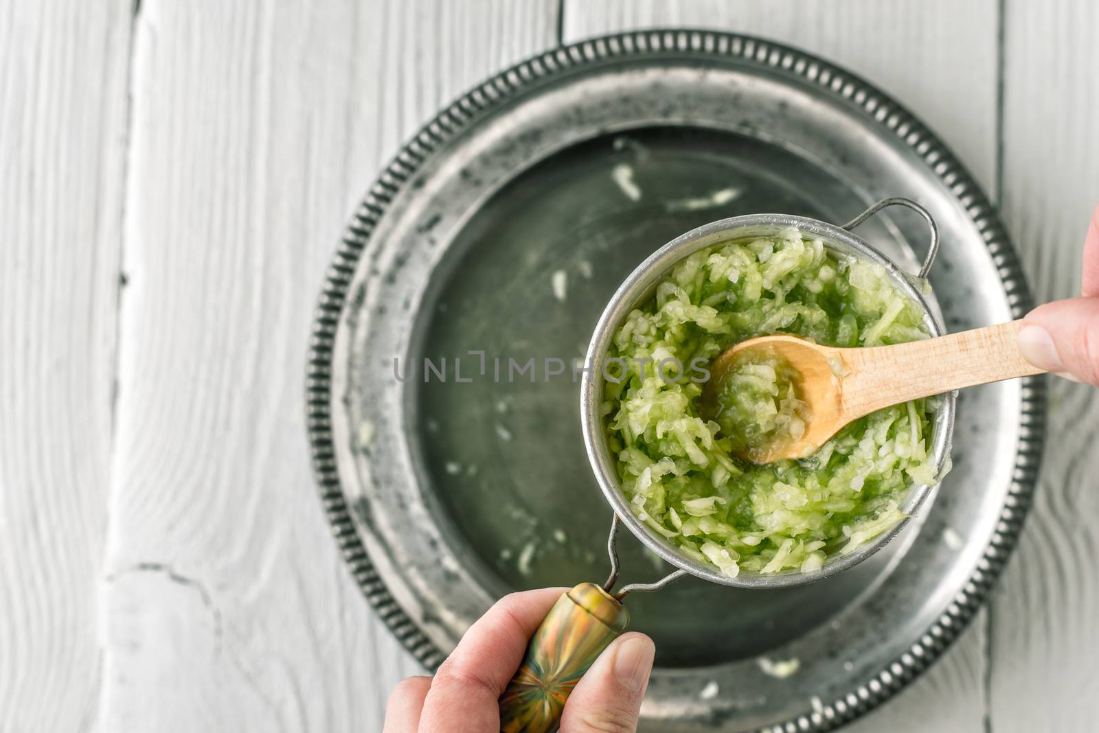 Grated cucumbers in the strainer with wooden spoon top view by Deniskarpenkov