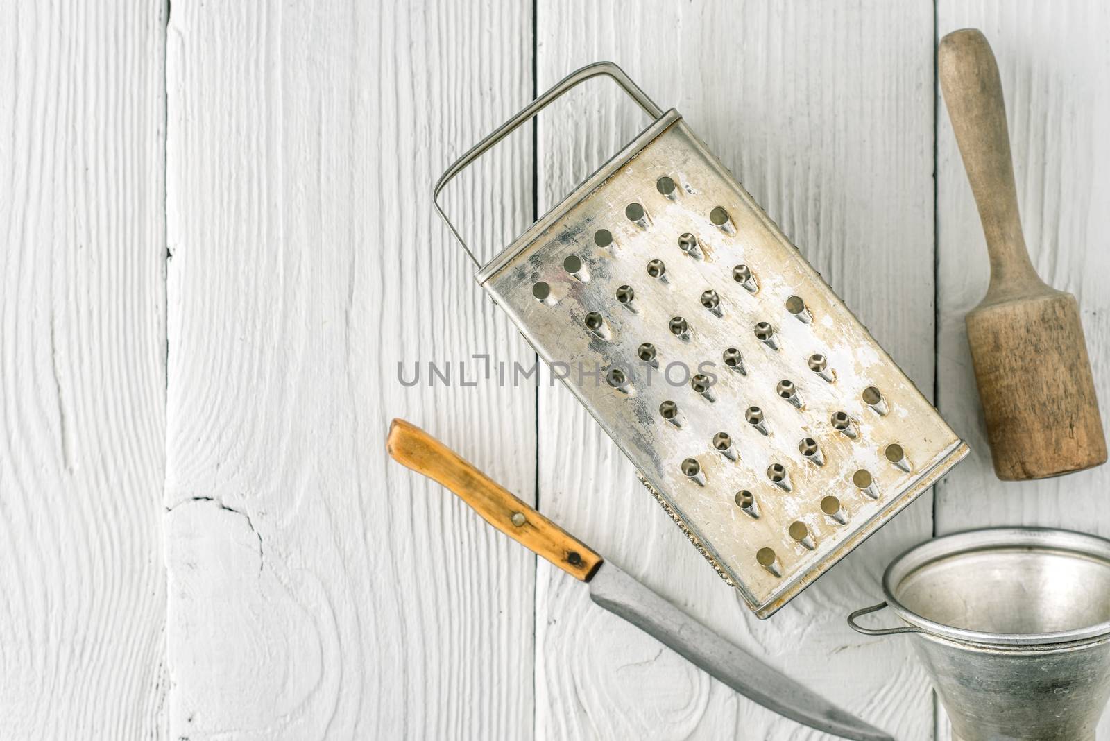 Grater, plunger , strainer and knife on the white wooden table top view by Deniskarpenkov