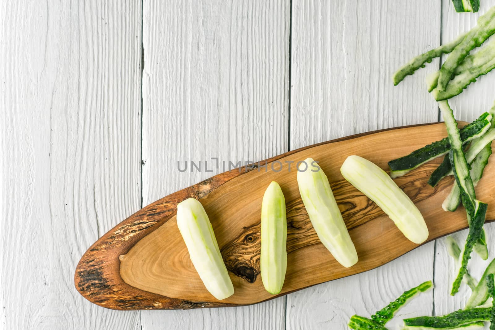 Peeled cucumbers on the wooden board  on the white table top view by Deniskarpenkov