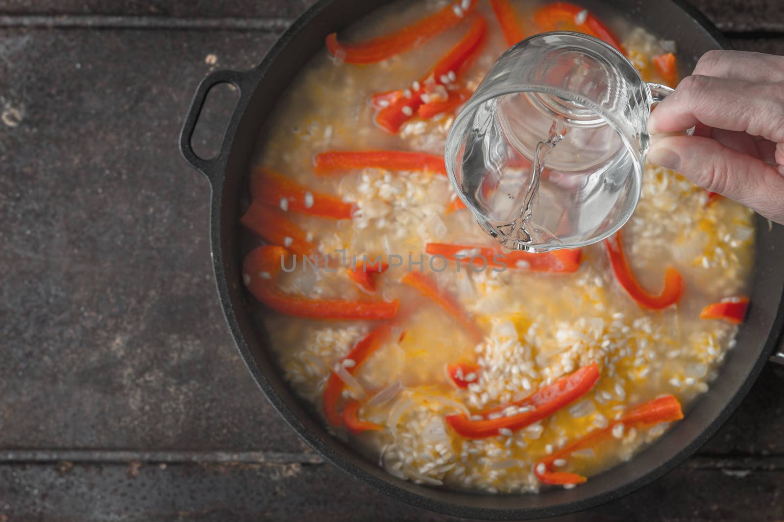 Adding water in the pan with rice and bell pepper top view by Deniskarpenkov