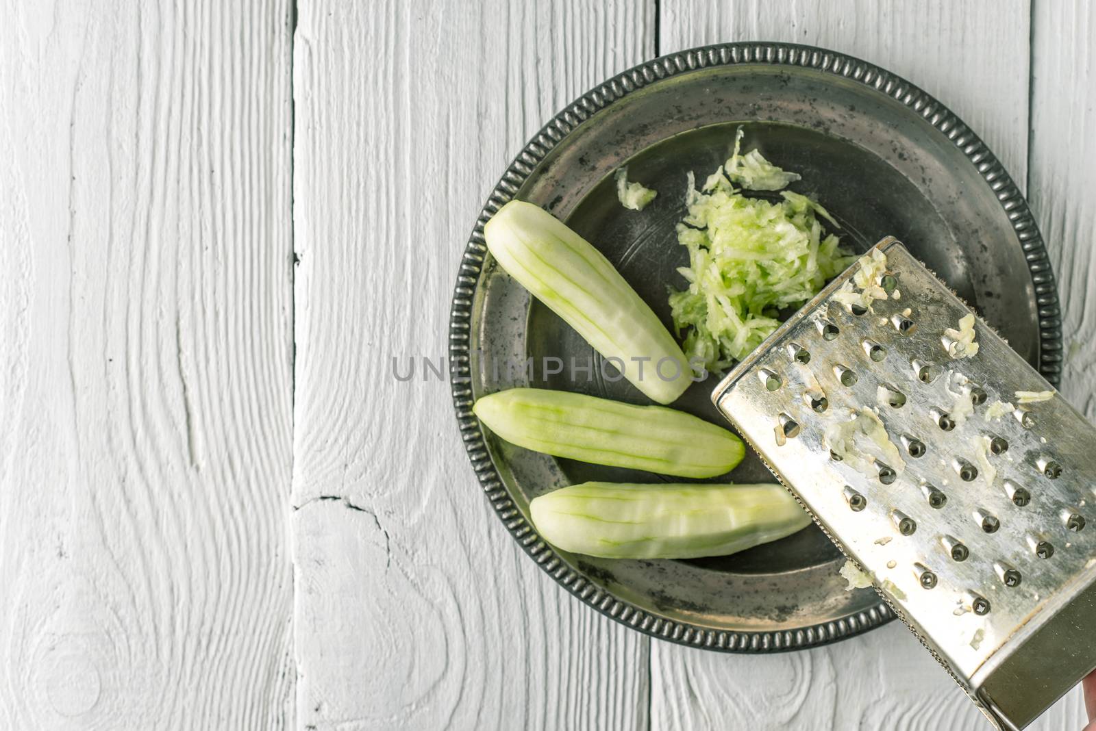 Grated and whole cucumber in the metal plate top view by Deniskarpenkov
