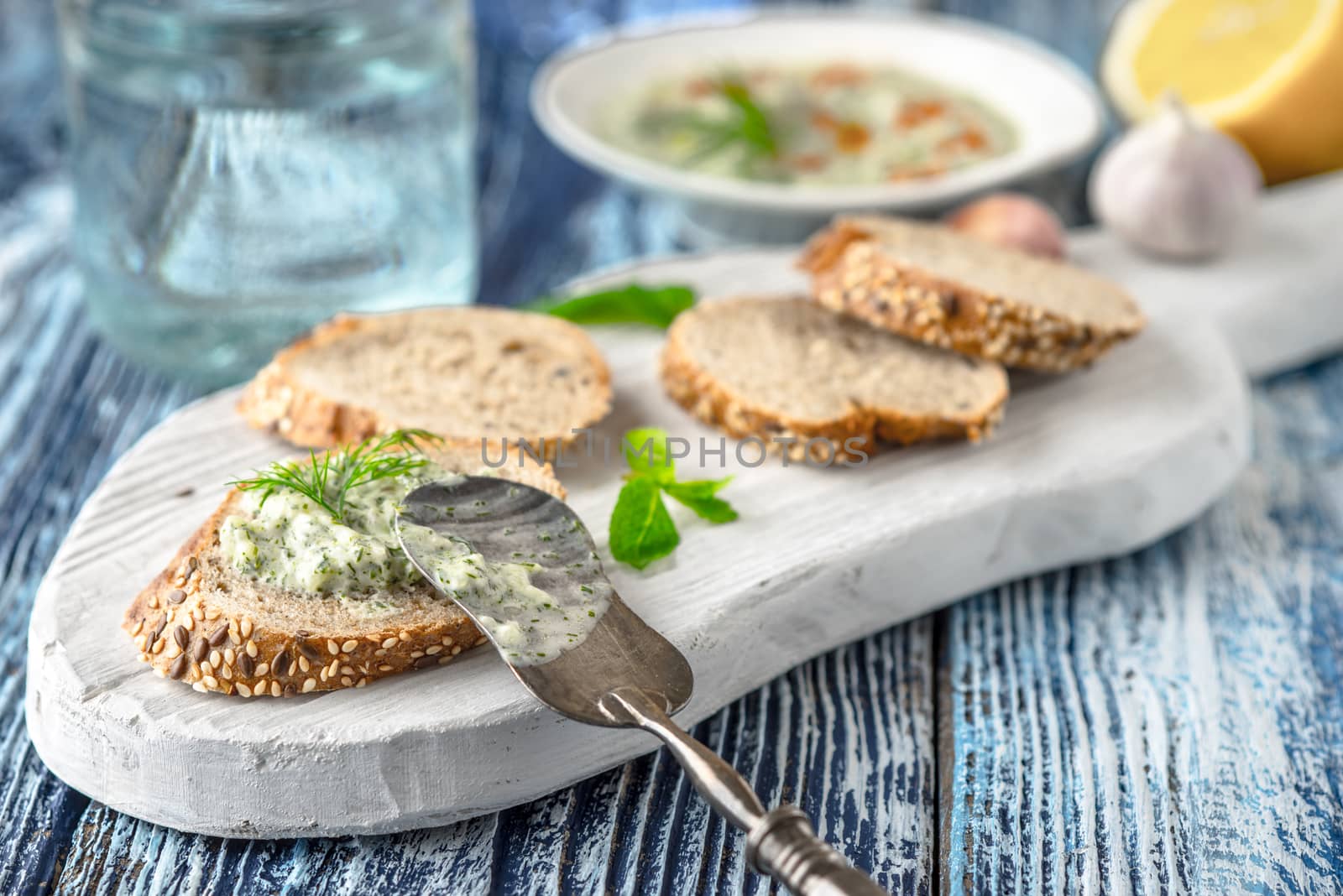 Bread with tzatziki on the white wooden board on the blue table horizontal by Deniskarpenkov