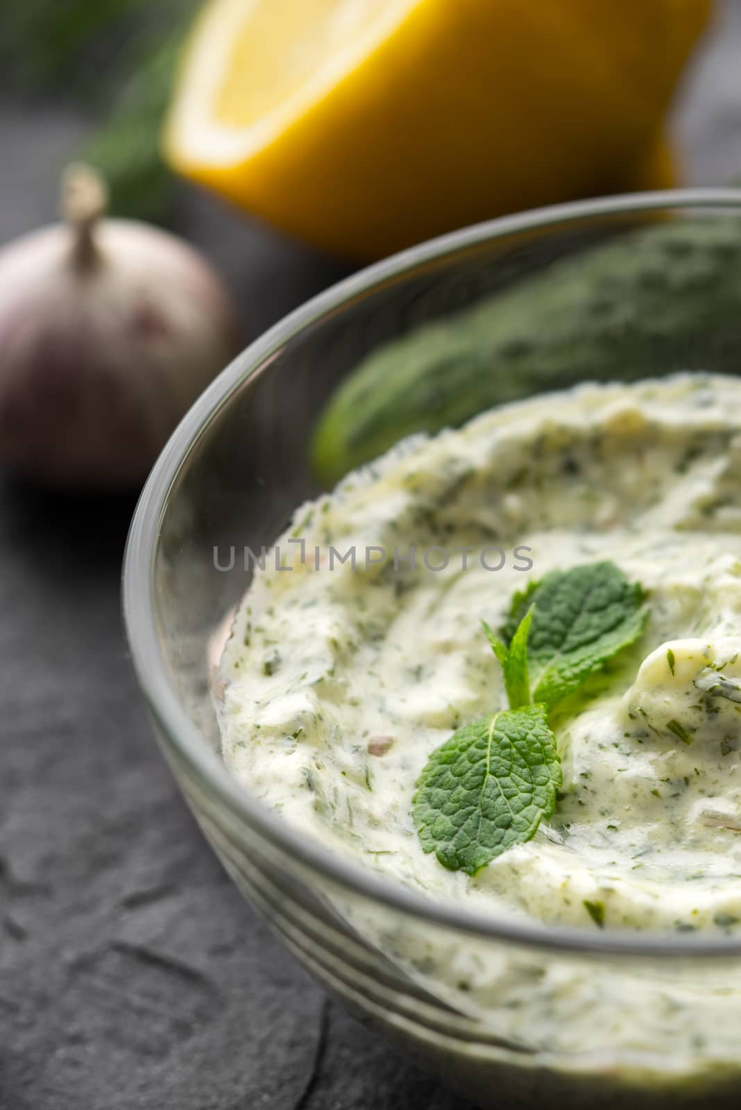 Tzatziki in the glass bowl on the black stone table vertical
