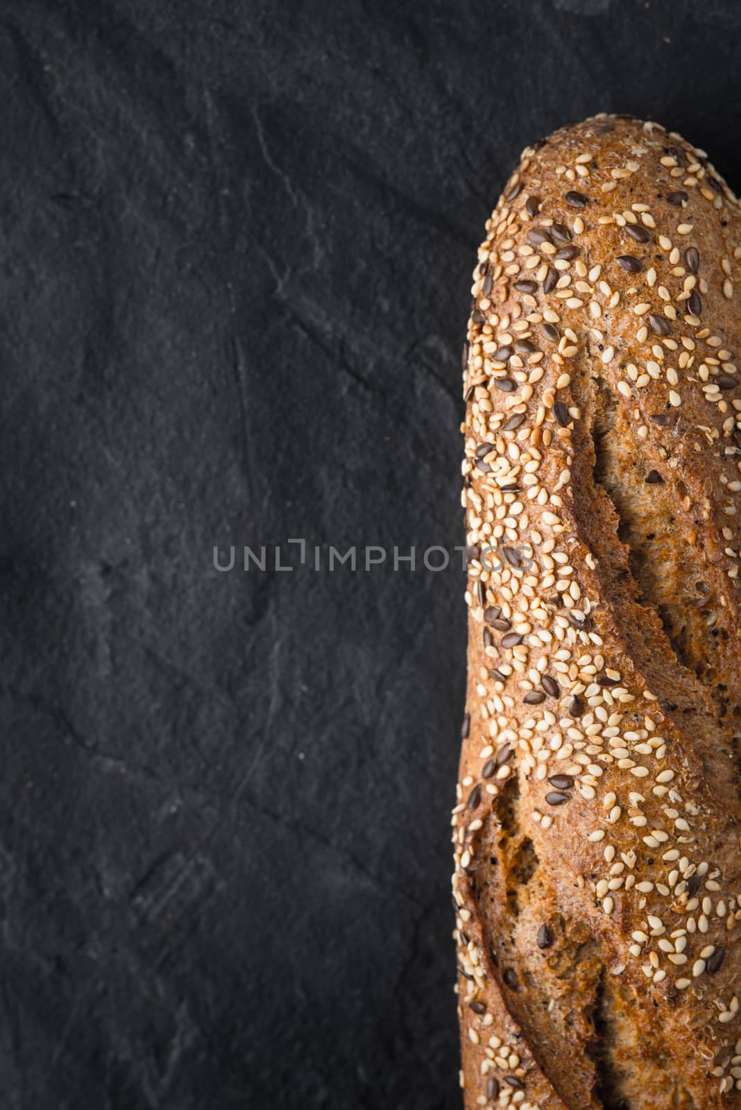 Bread with grains and seeds on the dark stone table vertical by Deniskarpenkov